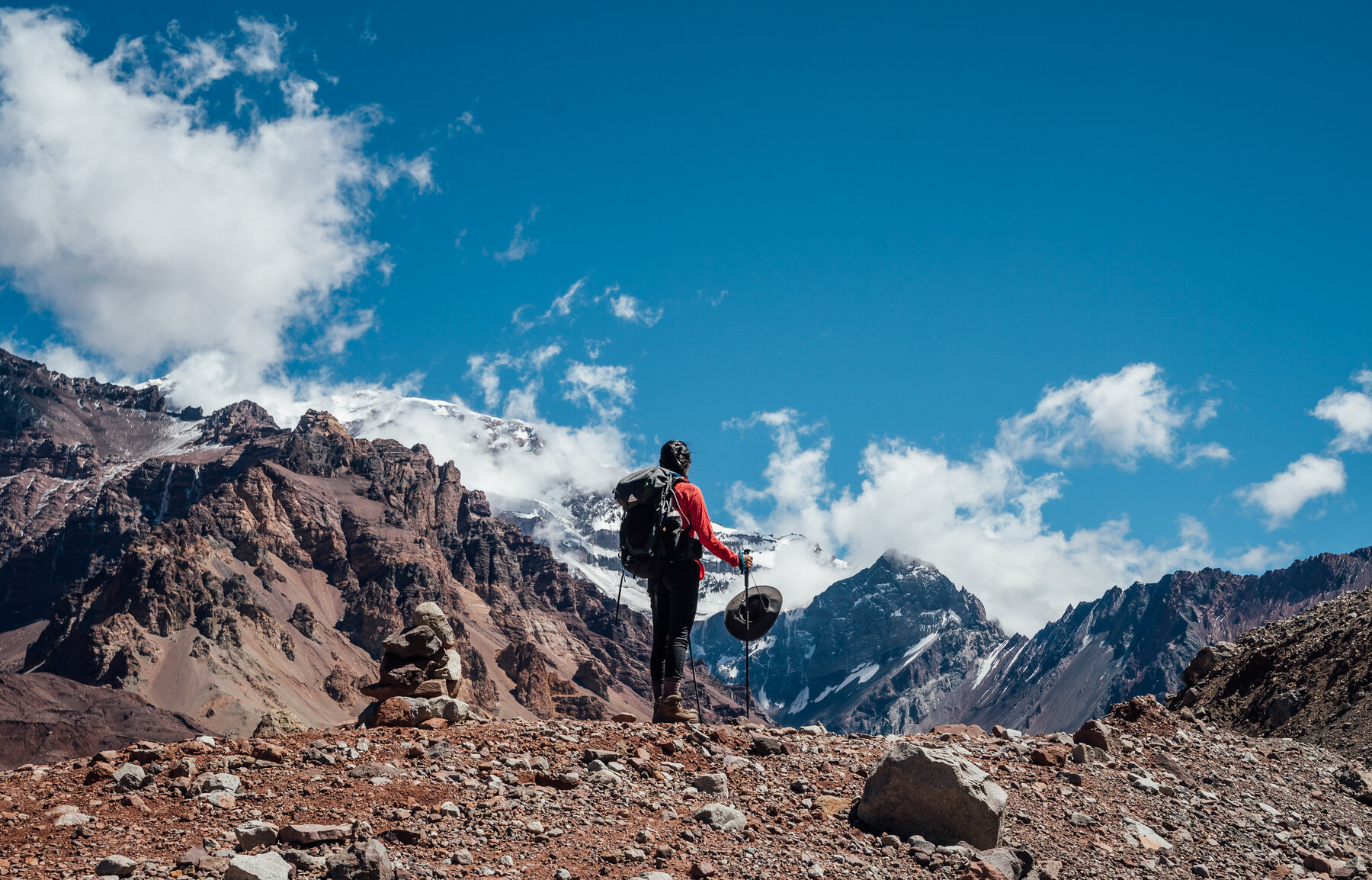 Climber in red jacket looking up at the snow-dusted summit of Aconcagua from the approach trail