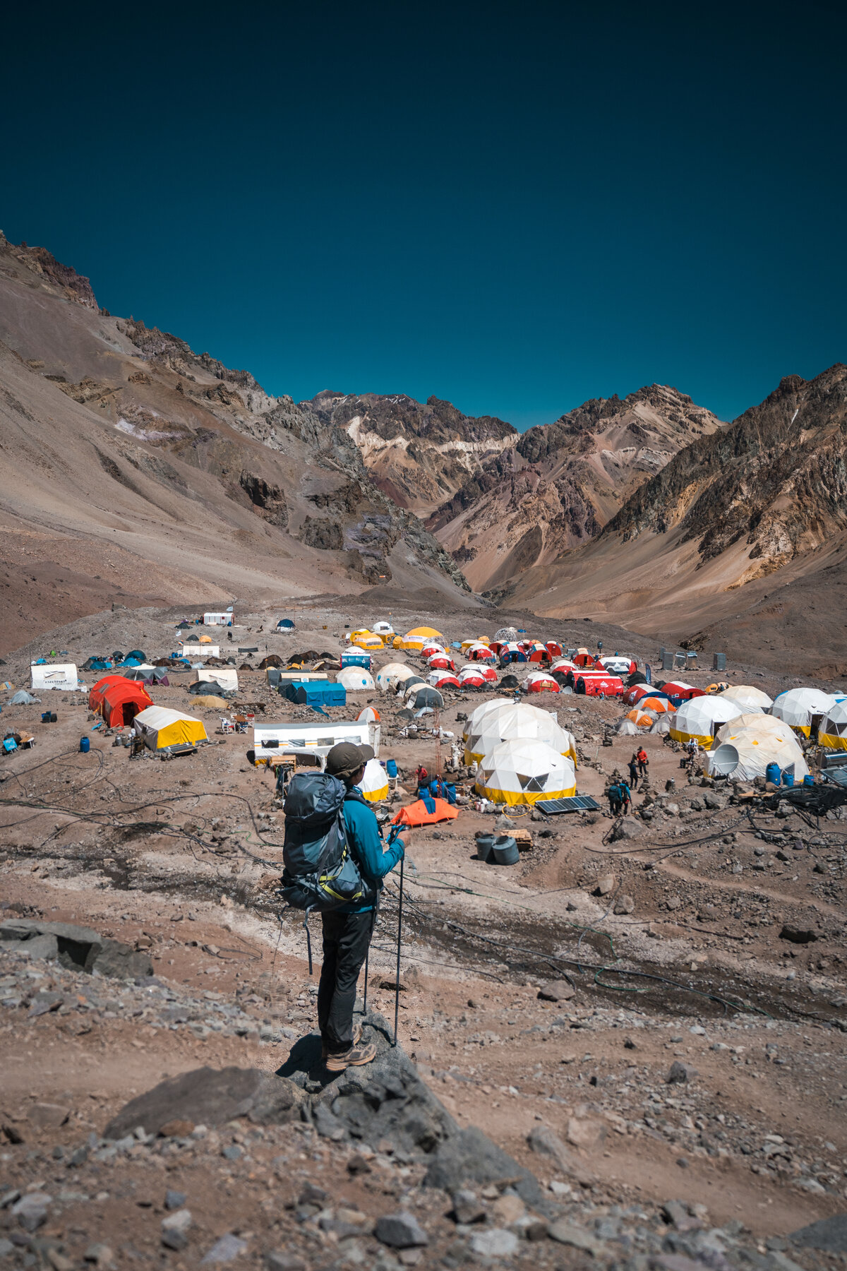 Climber standing on a ridge overlooking the sprawling Plaza de Mulas base camp below