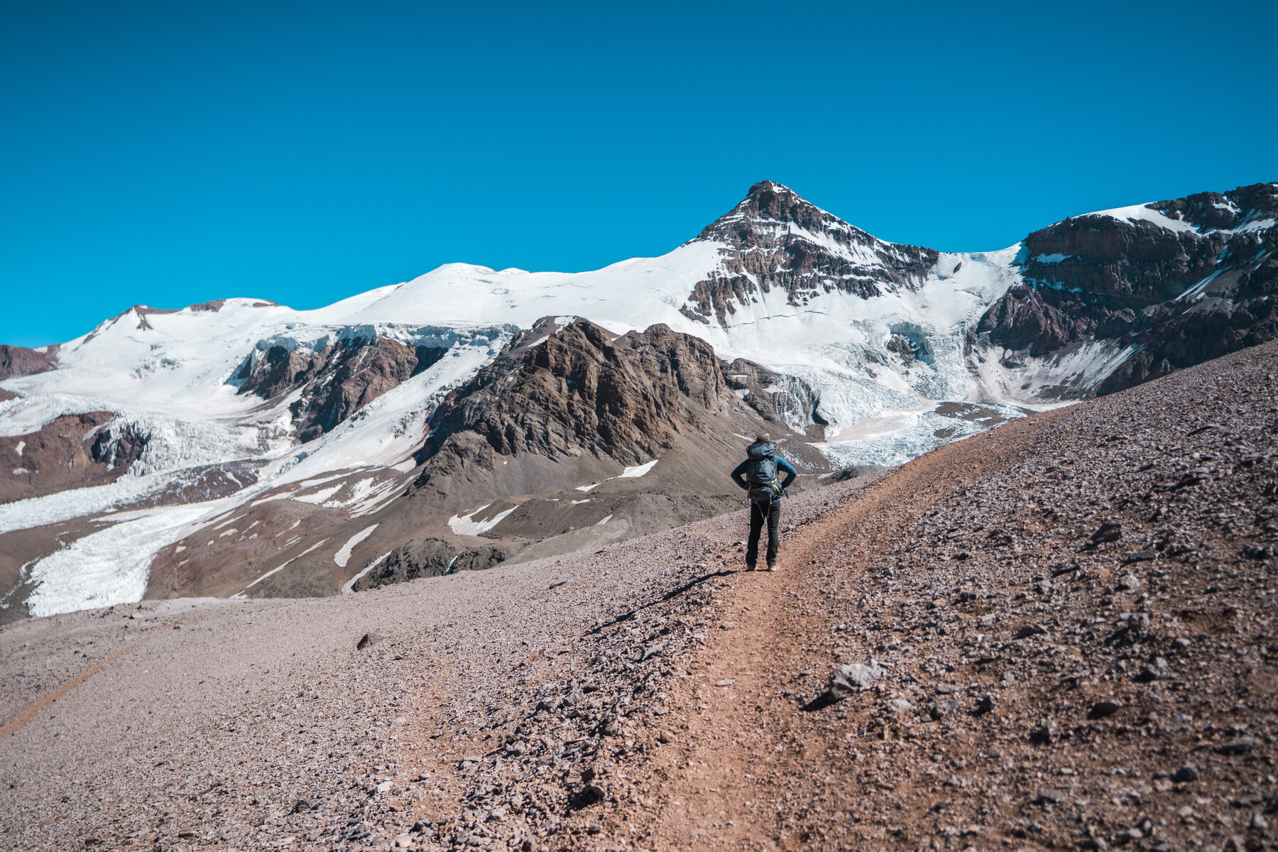 Climber on steep scree slope with glaciated peaks in background