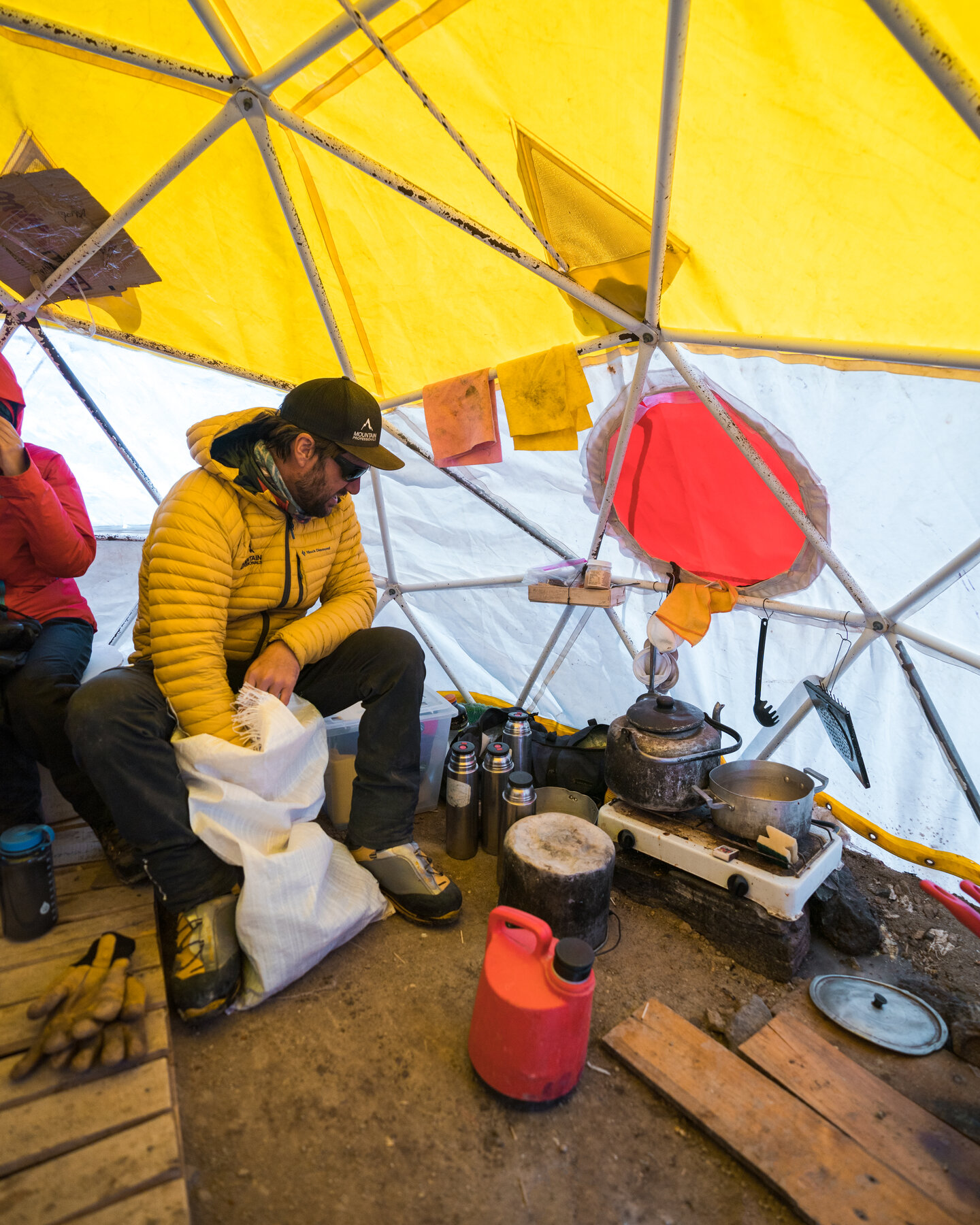 Expedition cook preparing a meal inside a yellow dome tent at high camp