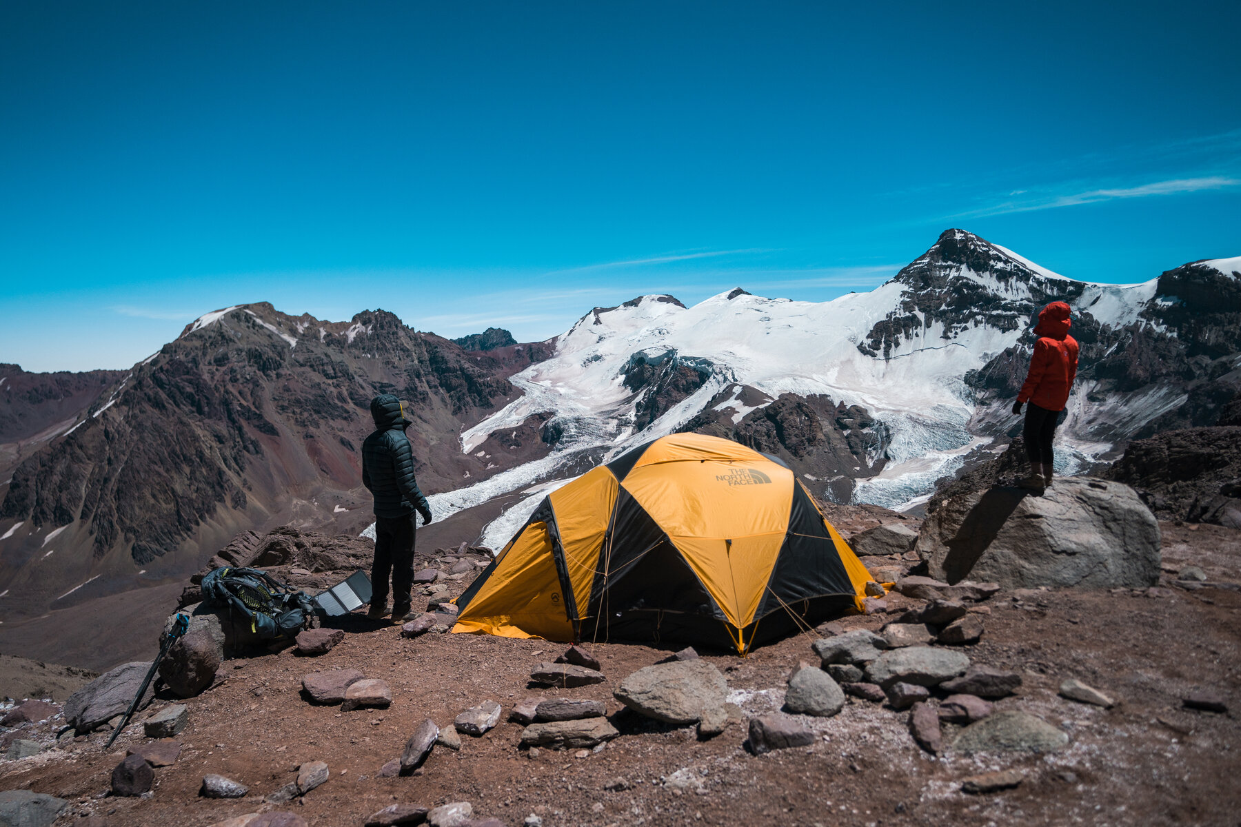 Two climbers at high camp with massive glaciated peaks behind