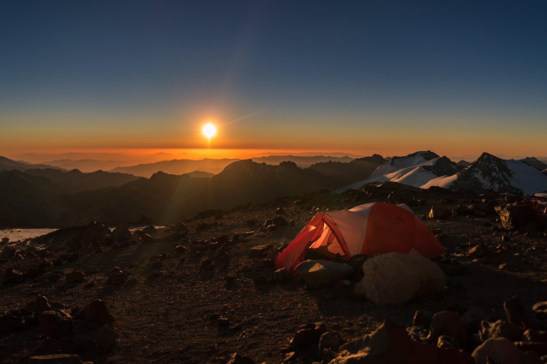 Glowing tent at sunset on Aconcagua with the sun setting over silhouetted mountain ridges