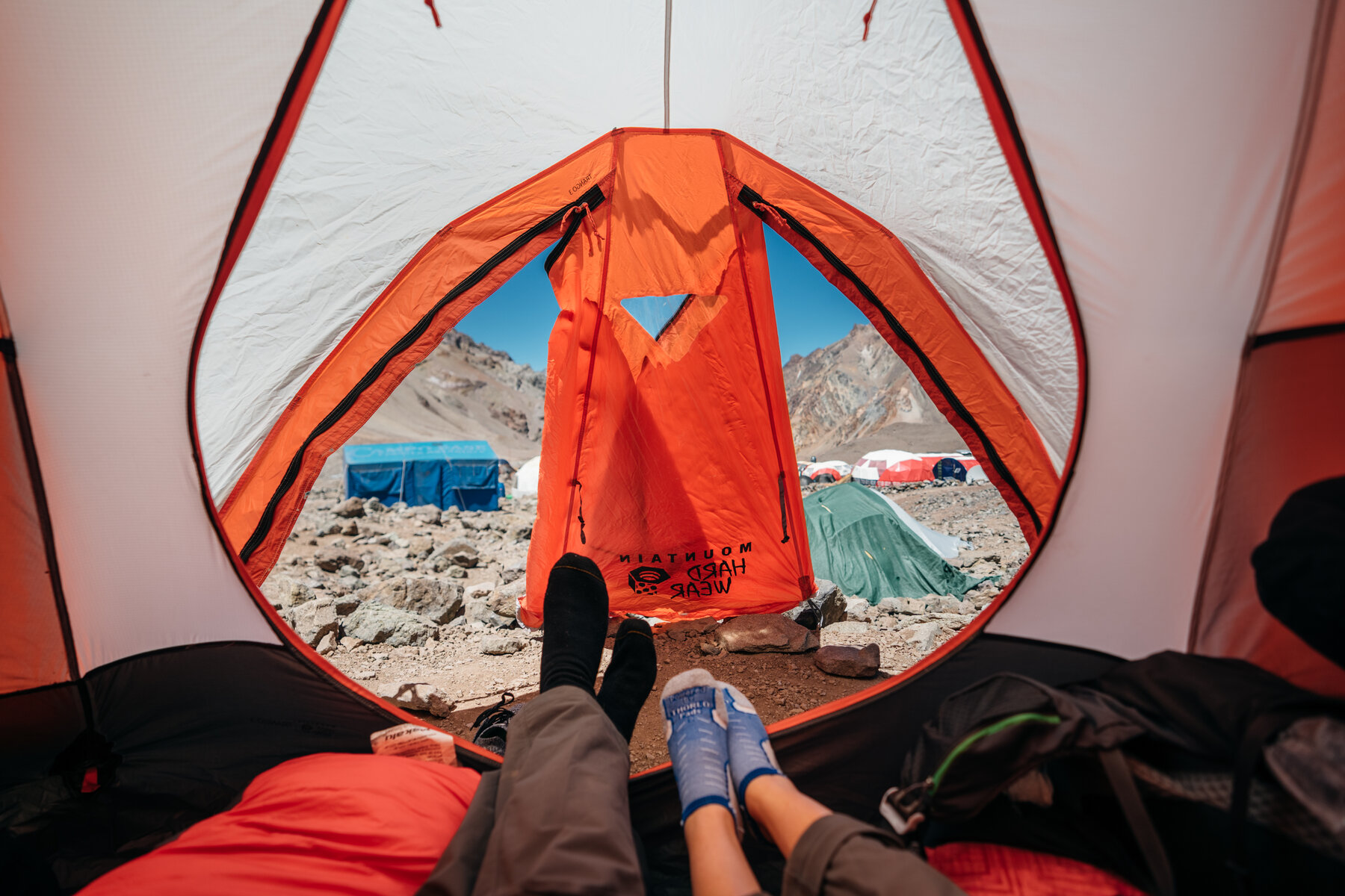 View from inside an orange tent looking out at other tents and mountains at base camp
