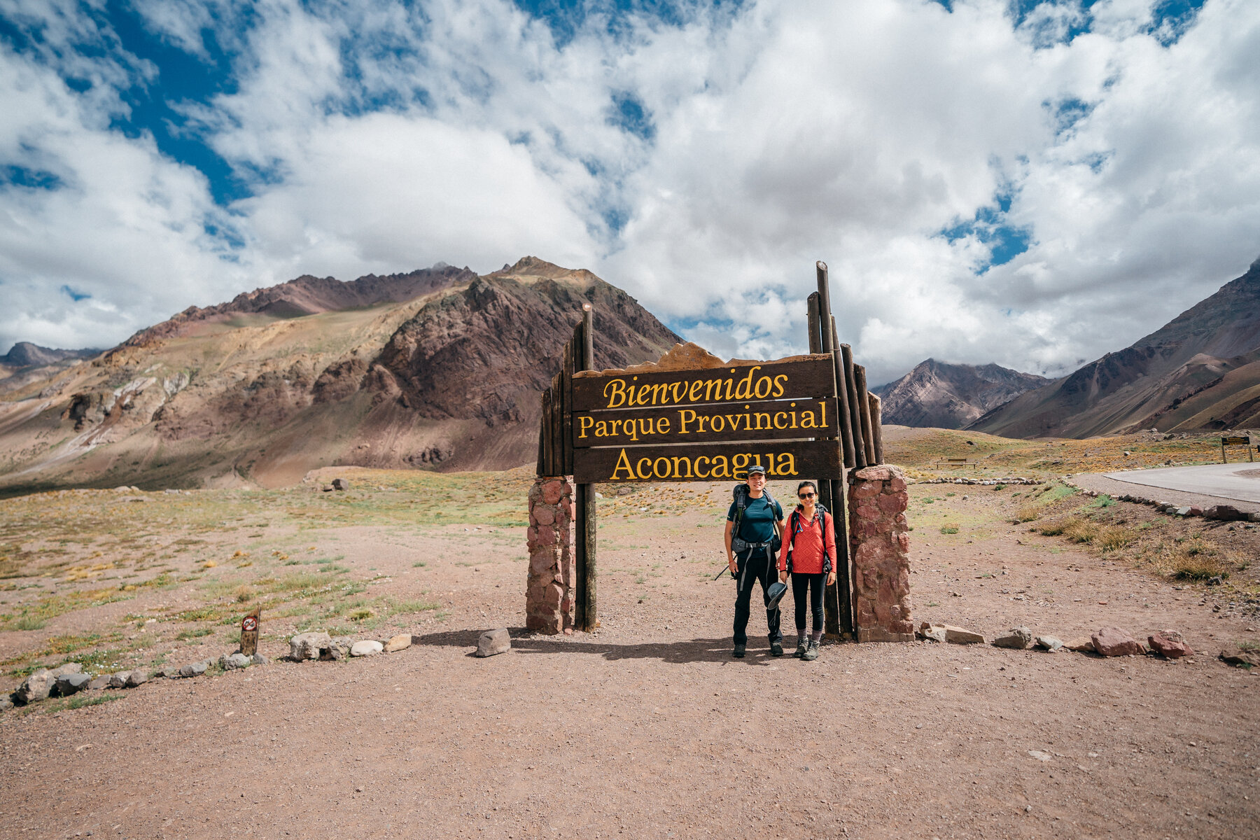 Jason and Grace at the Aconcagua Provincial Park entrance sign with snow-capped peaks behind