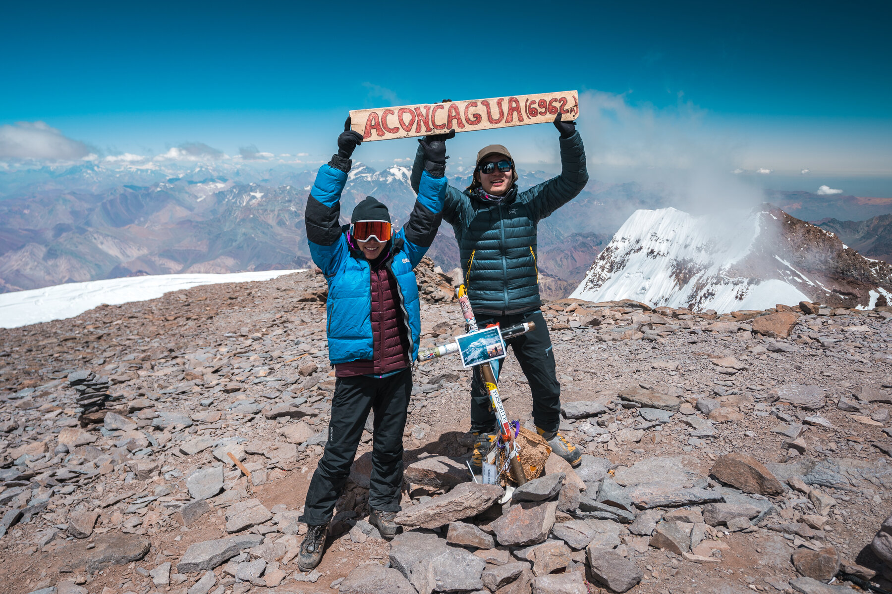 Jason and Grace holding the Aconcagua 6962 summit banner with arms raised
