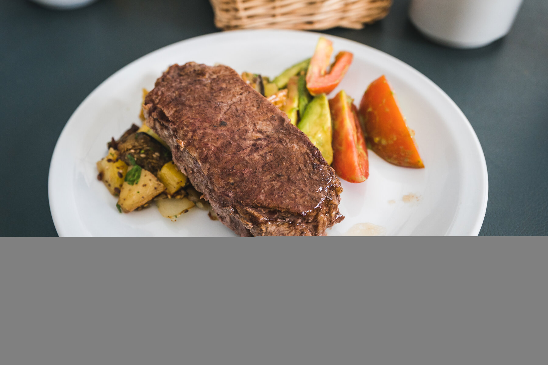 Argentine steak with roasted potatoes and sliced tomato on a white plate — Mendoza pre-expedition dinner