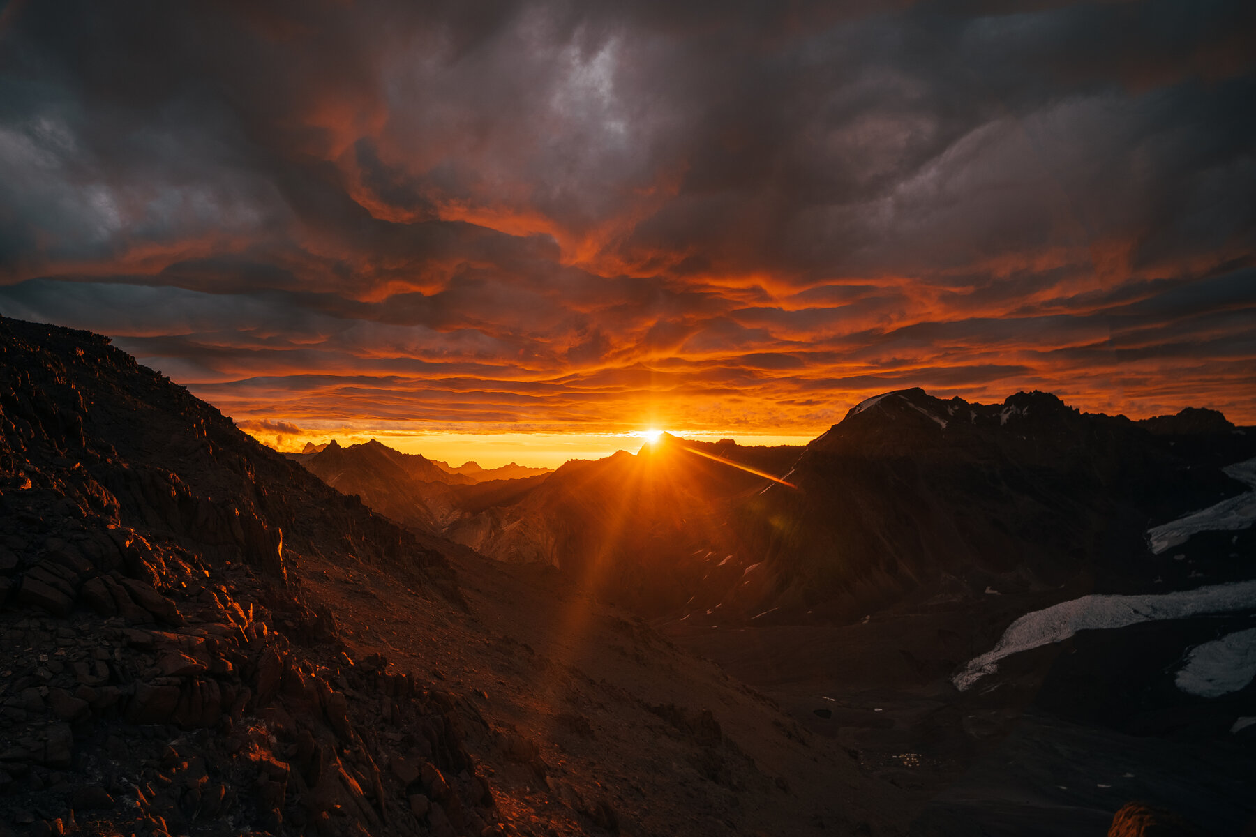 Fiery sunrise over the Andes with dramatic orange and red clouds above mountain silhouettes