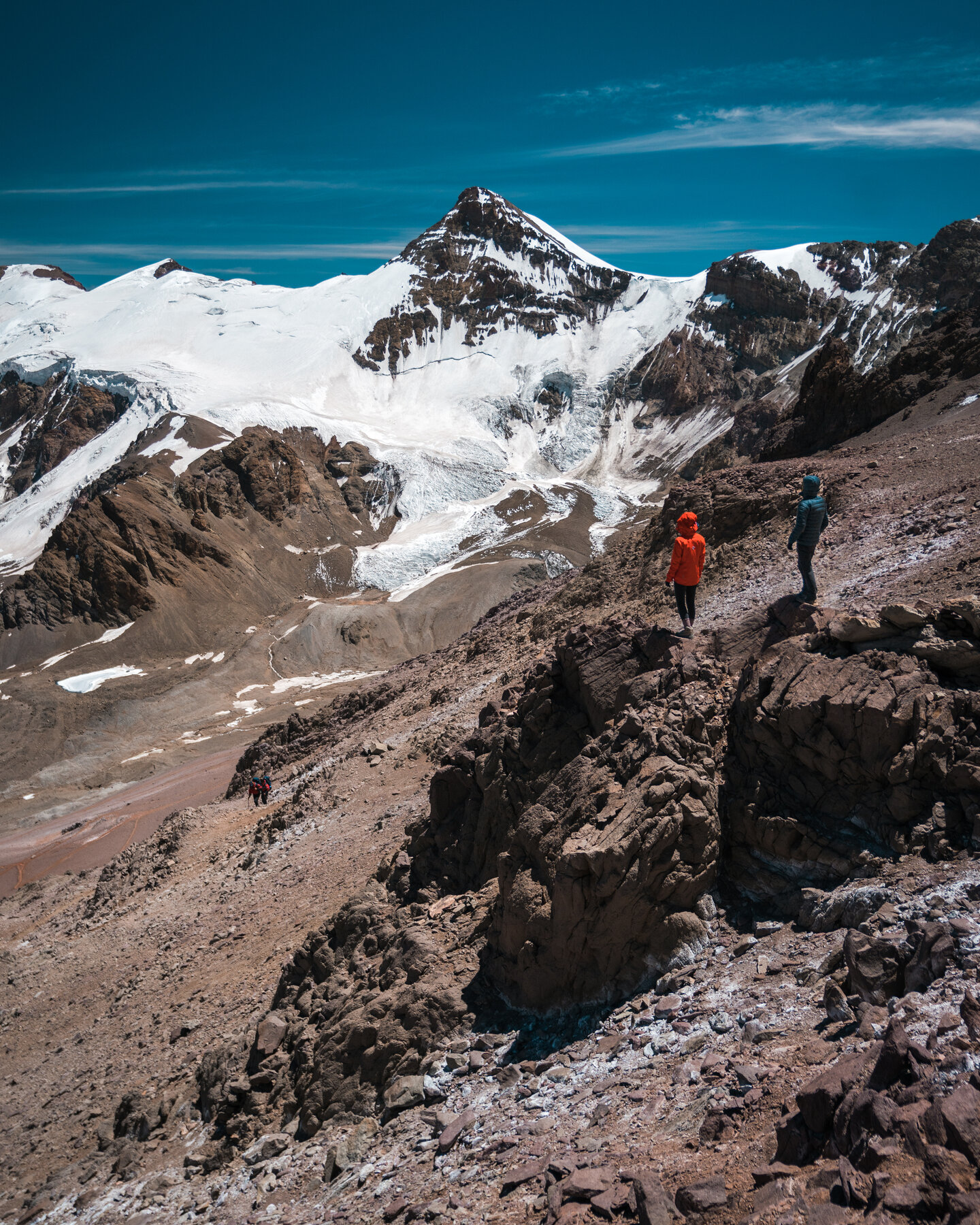 Two climbers standing on a rocky ridge with glaciated Aconcagua peaks towering behind