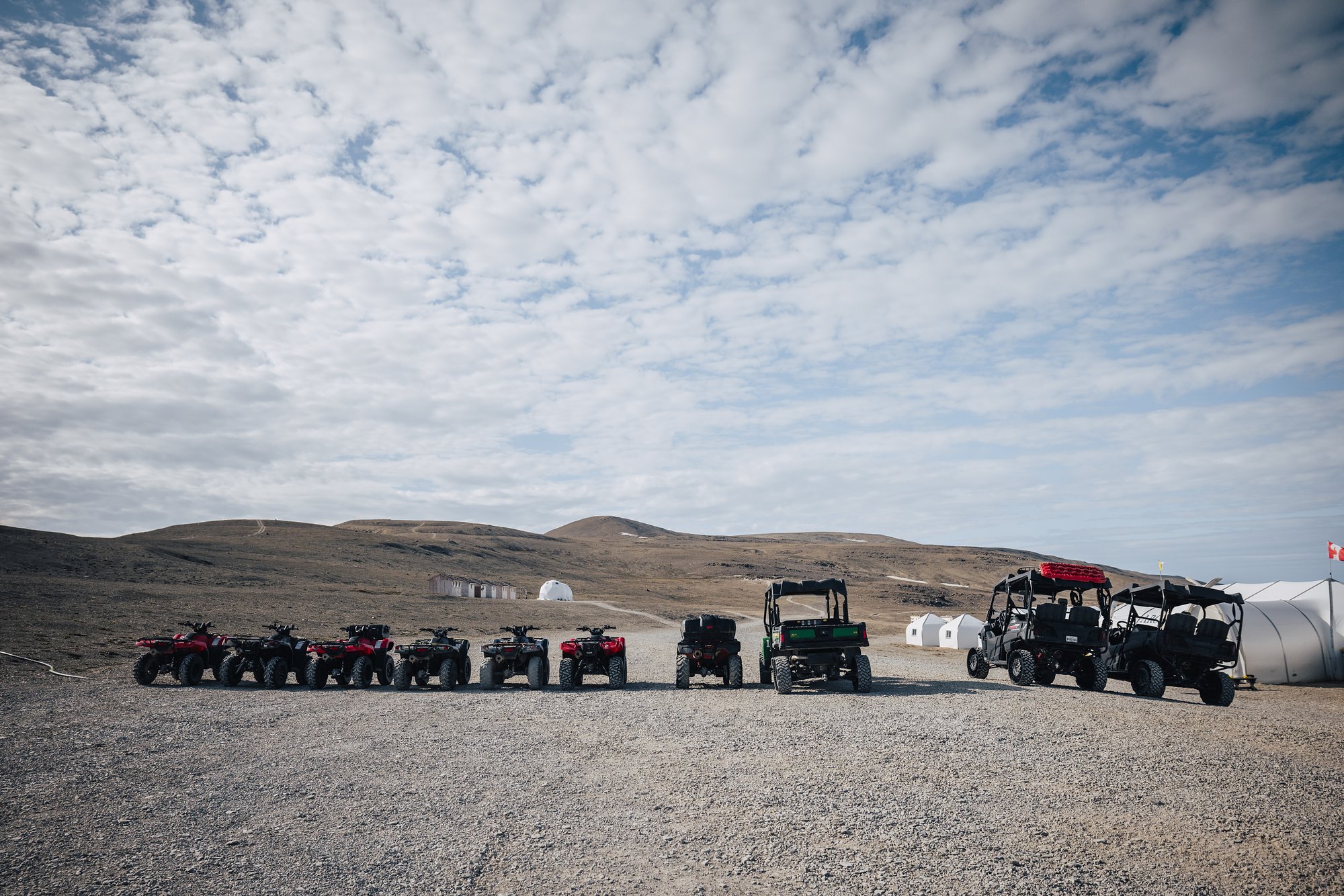A row of ATVs and side-by-side buggies lined up on the gravel at Arctic Watch