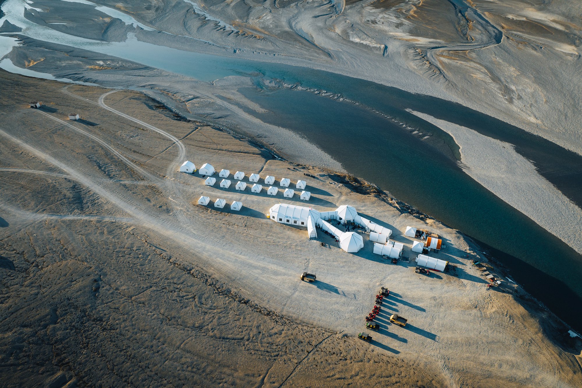 Arctic Watch from above: rows of white guest cabins, the main lodge and a line of ATVs beside the river