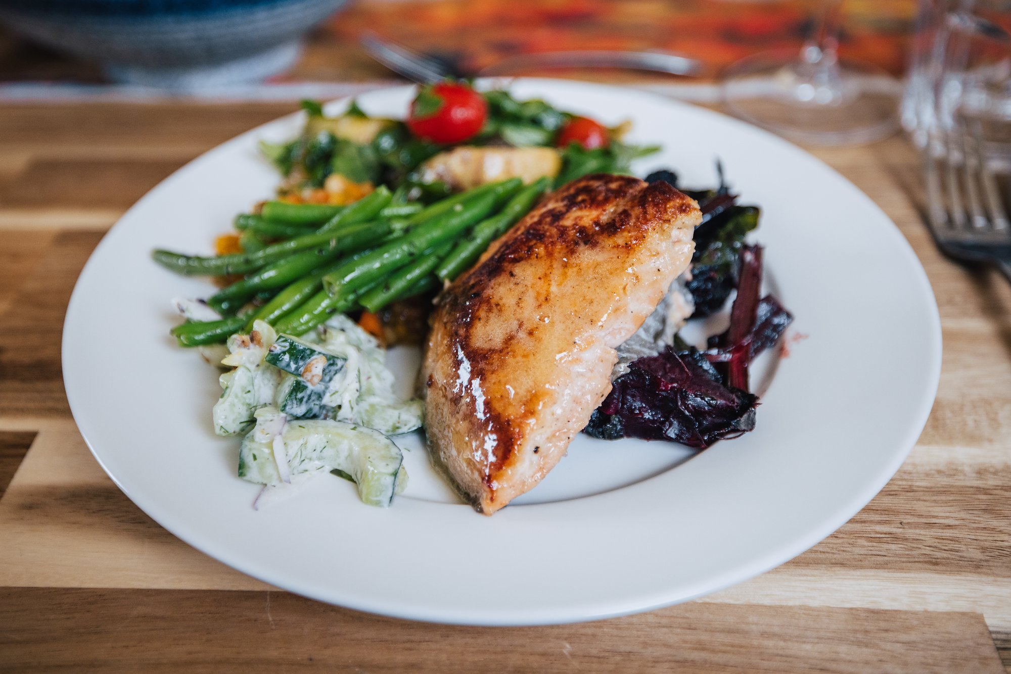 A plate of seared fish with green beans, tomato salad, cucumber salad and beets