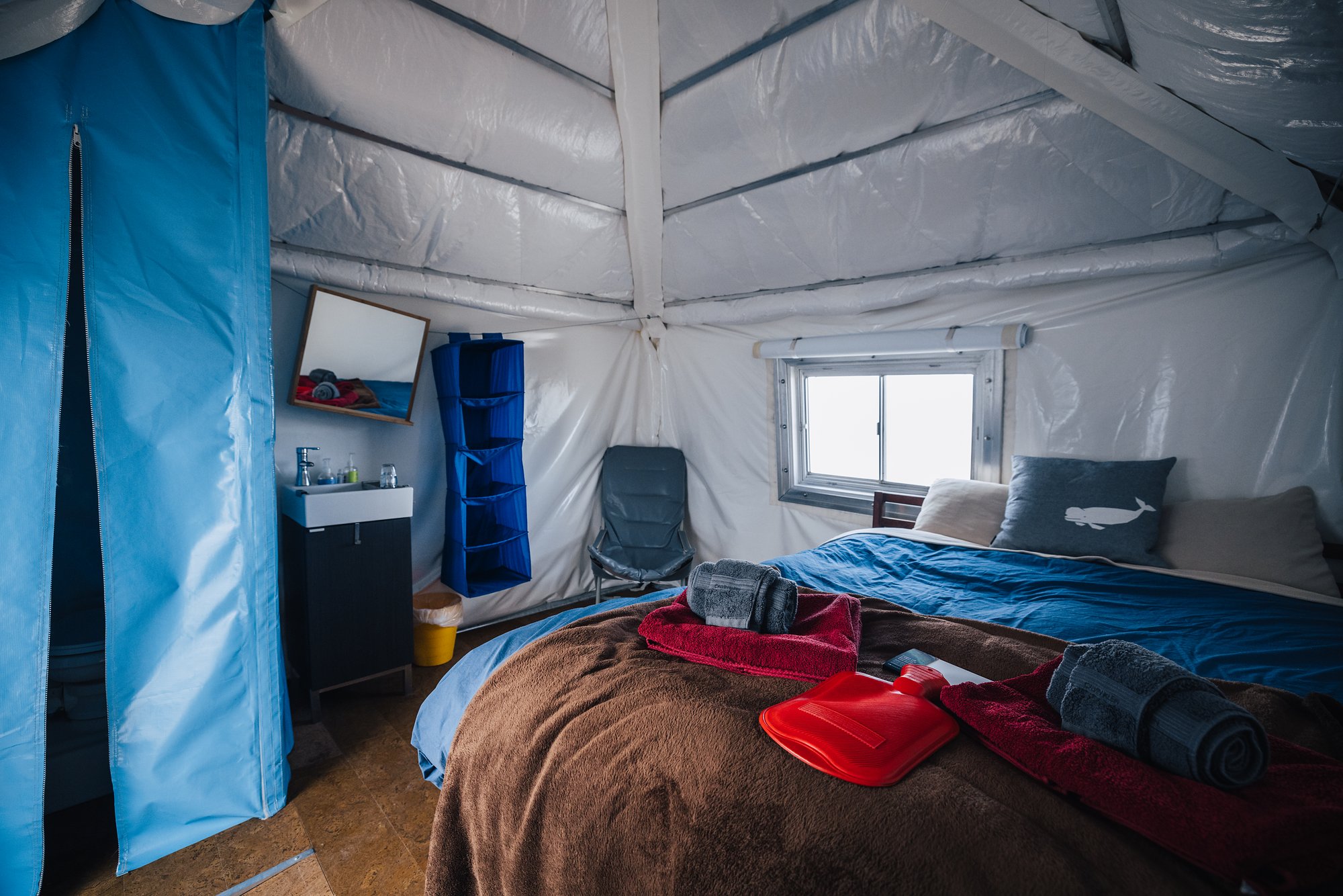 Inside a guest cabin at Arctic Watch: a double bed with towels, a red hot-water bottle and a beluga pillow