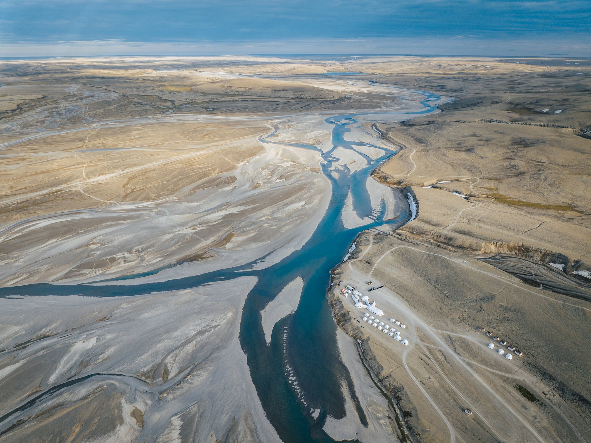Aerial view of Arctic Watch's white tents on the bank of the braided Cunningham River, tundra running to the horizon