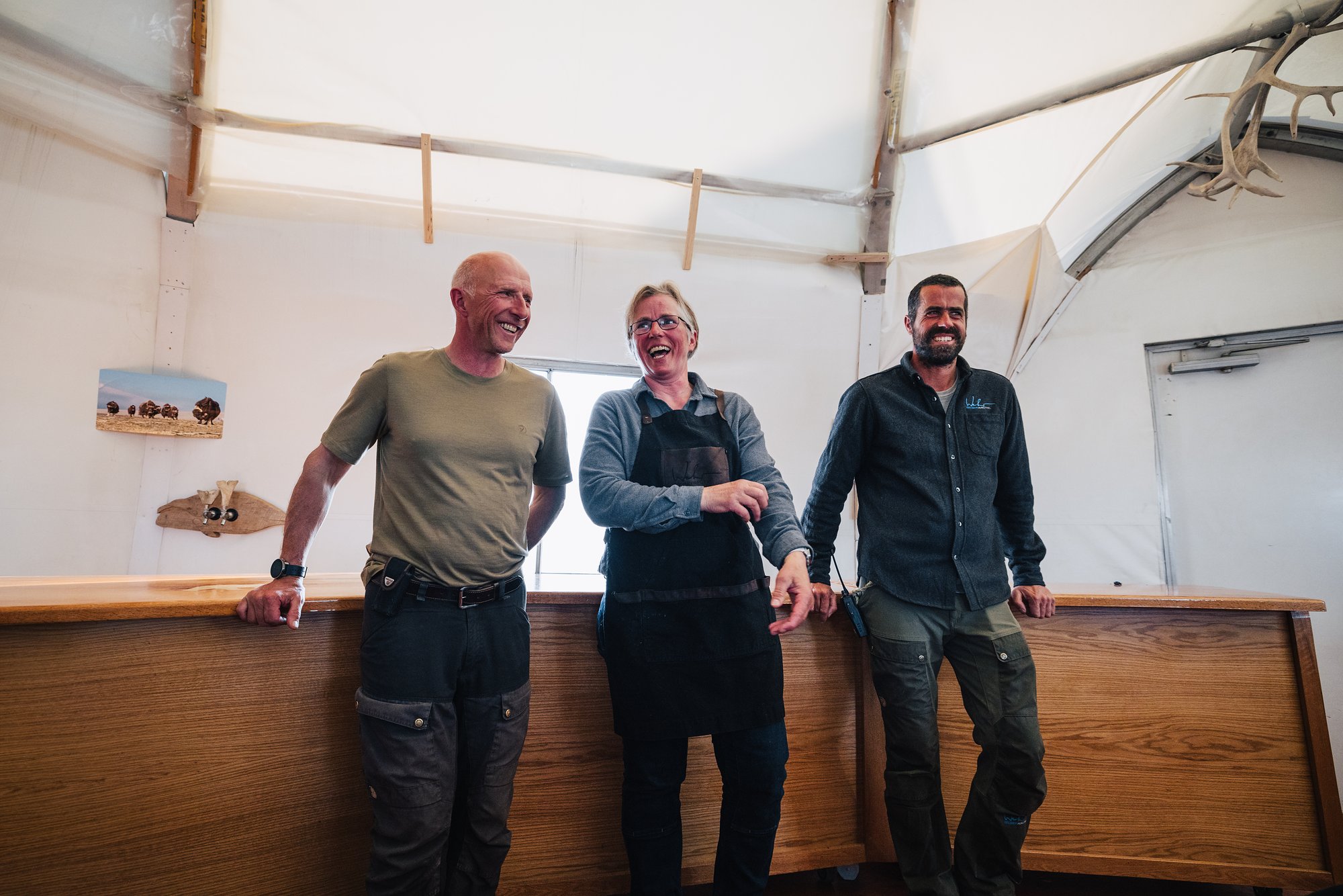 Three of the Arctic Watch team laughing behind the wooden bar in the main lodge