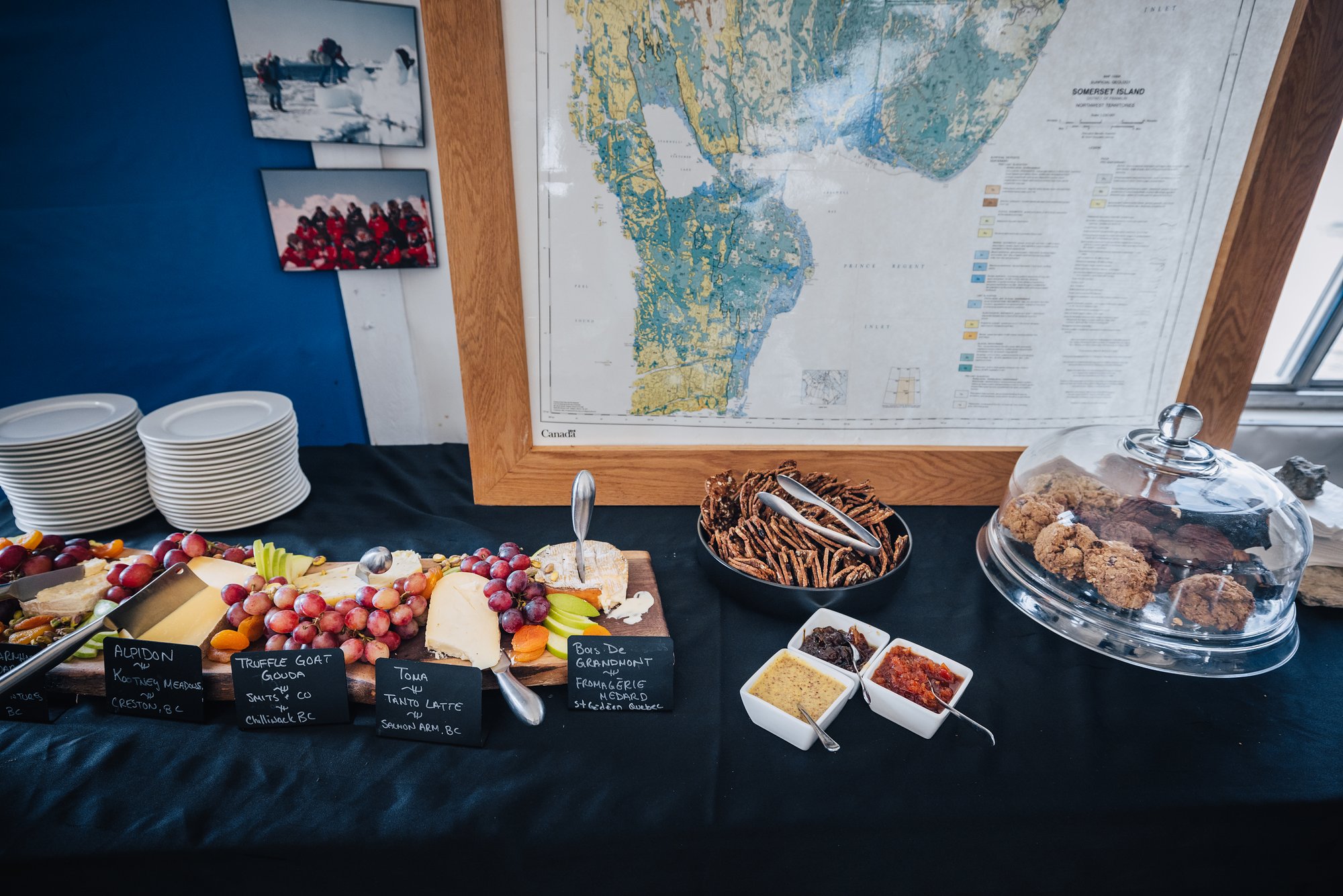 An afternoon spread in the lodge: cheese board, grapes, charcuterie and cookies under a glass dome