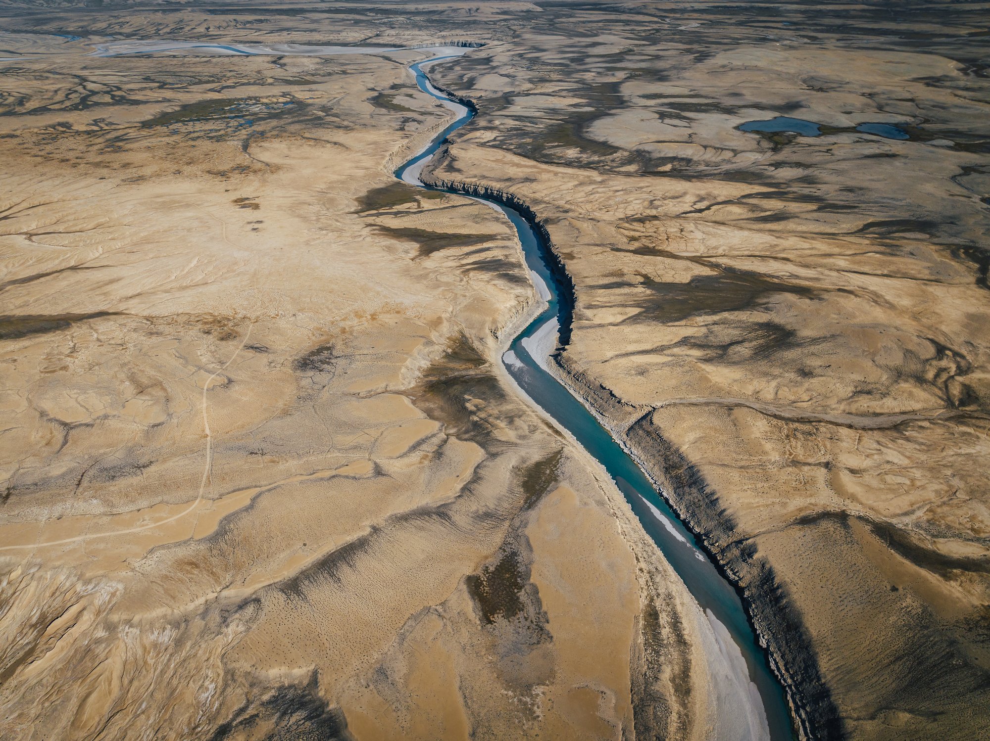 Aerial view of a river channel cutting a clean line through tan tundra