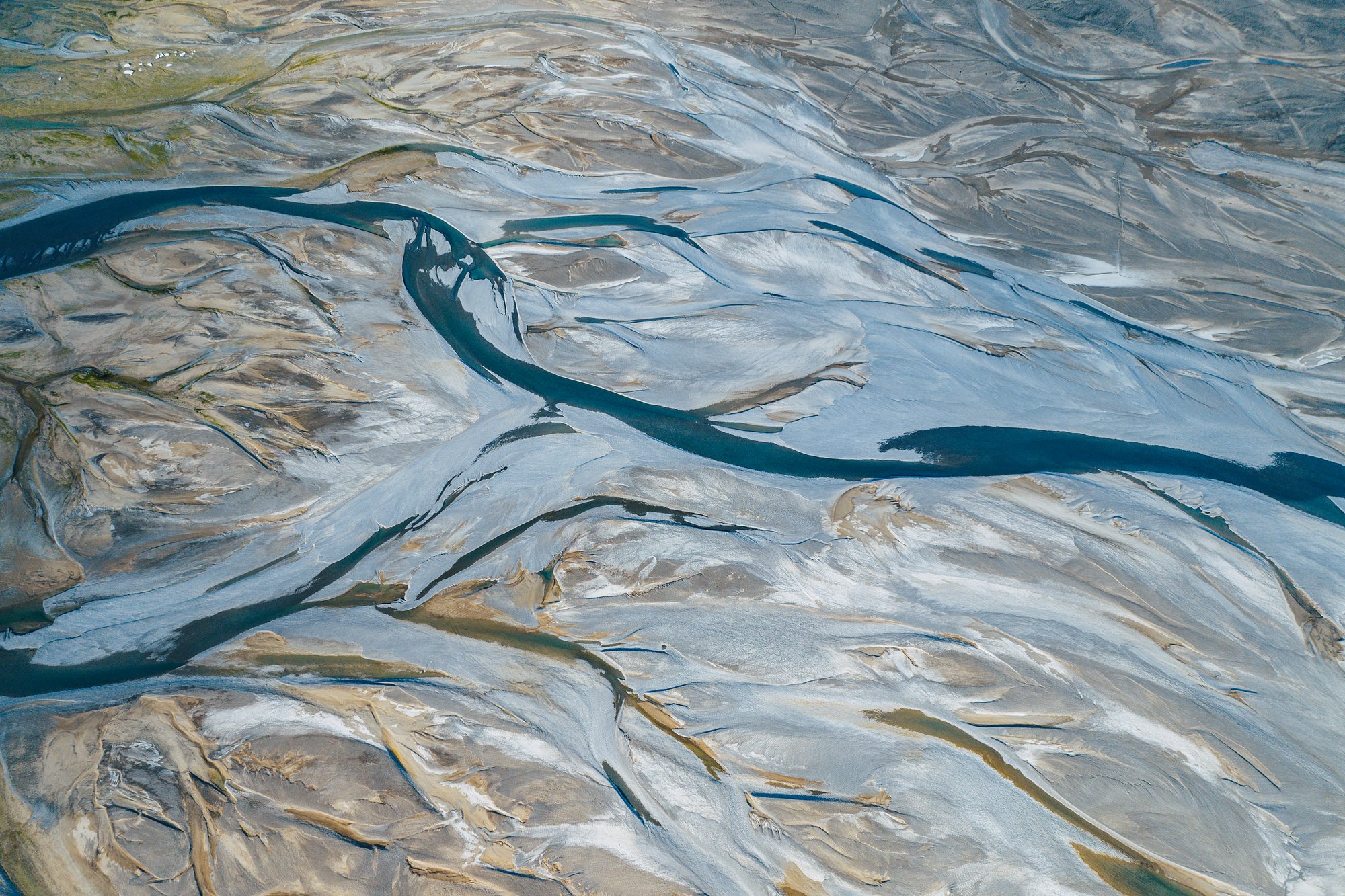 A dark blue river channel snaking between silver and tan gravel bars, seen from above