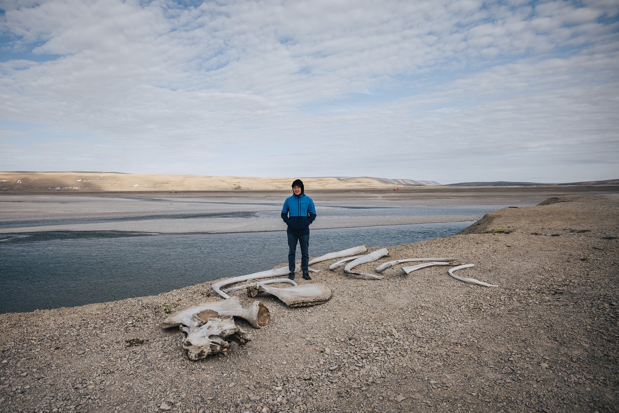 Grace standing among whale bones laid out on the gravel riverbank near the lodge