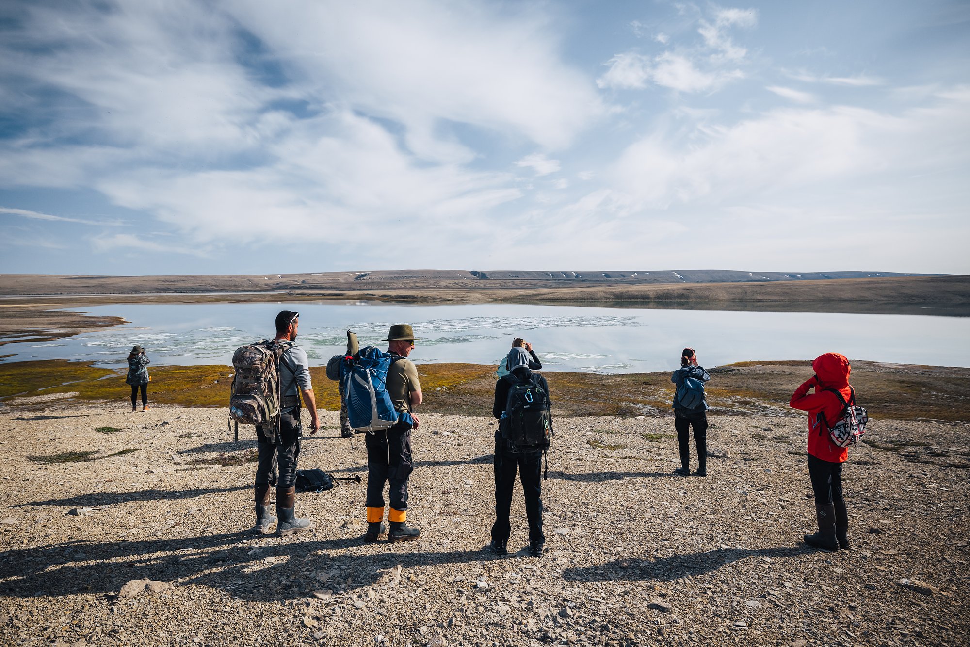 Hikers with backpacks on the gravel shore looking out at an ice-choked bay