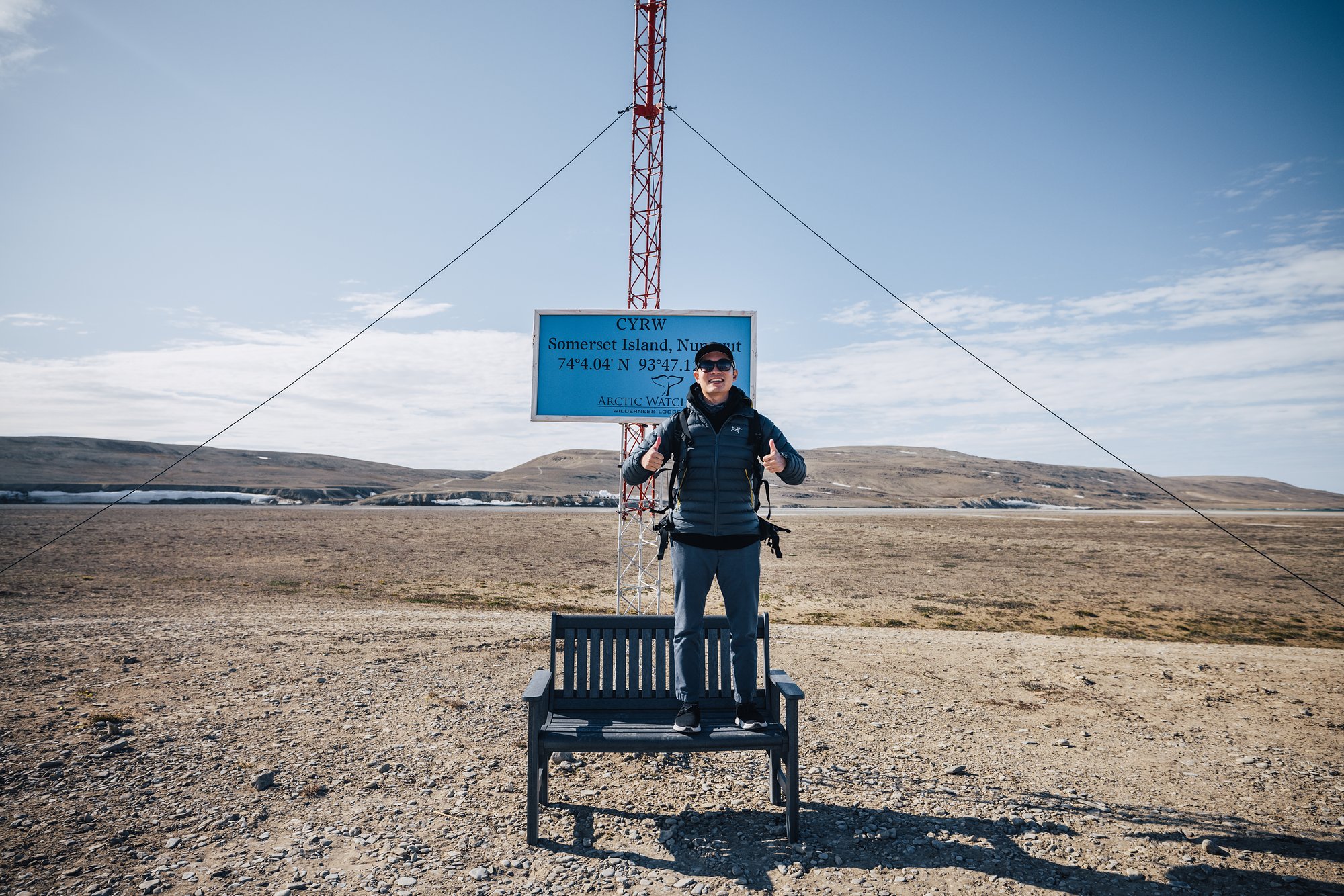 Jason standing on the bench beneath the CYRW airstrip sign and windsock