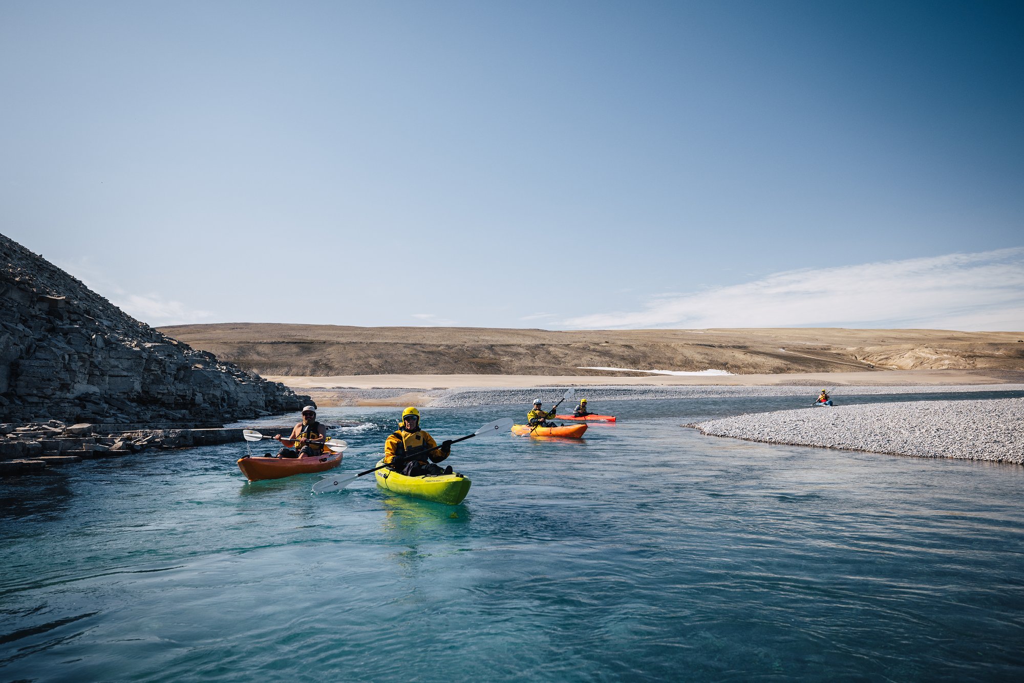 Kayakers in yellow and orange boats paddling down the Cunningham River beneath a low cliff