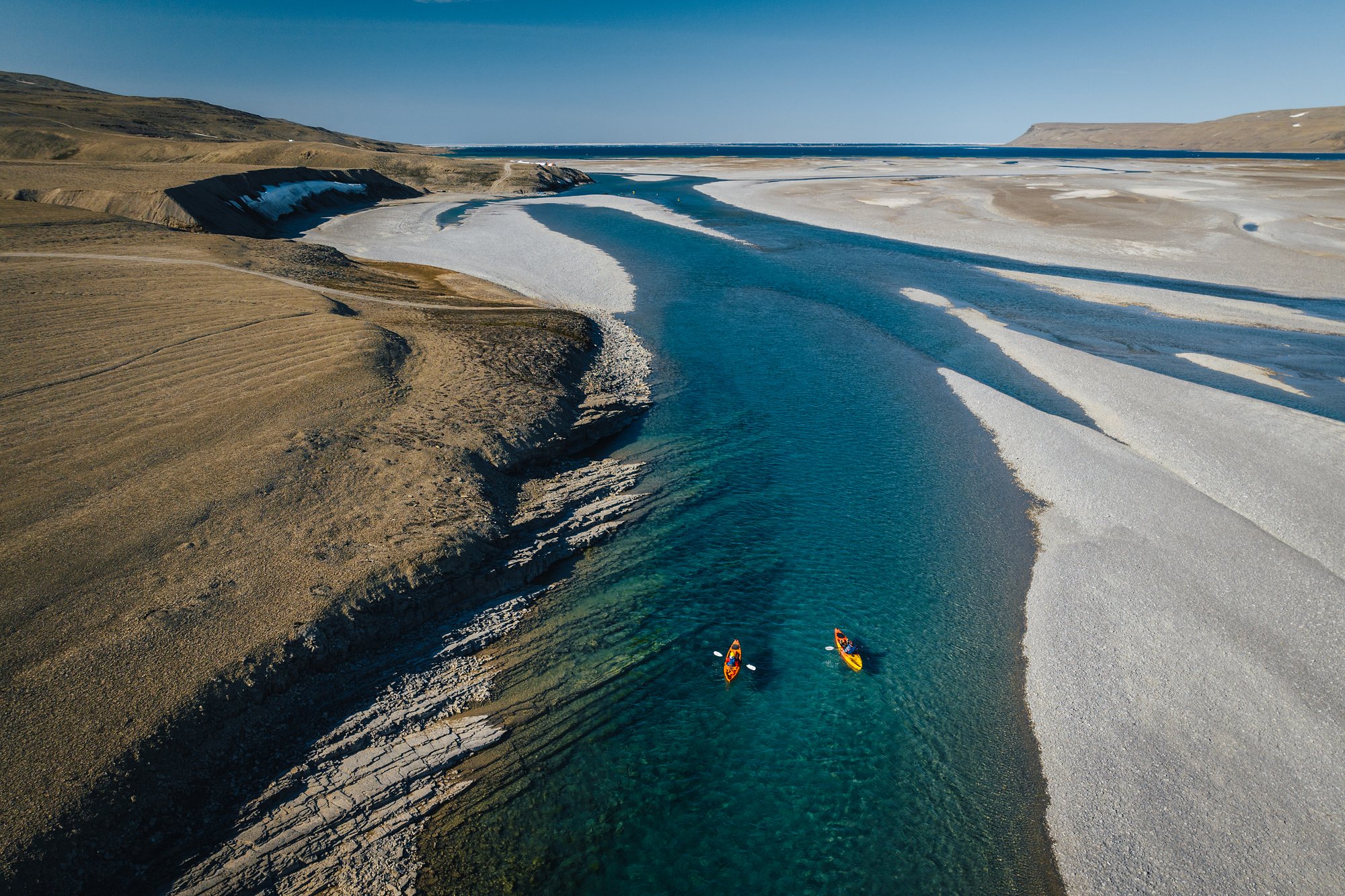 Aerial view of a yellow and an orange kayak paddling down a teal channel of the Cunningham River between white gravel banks