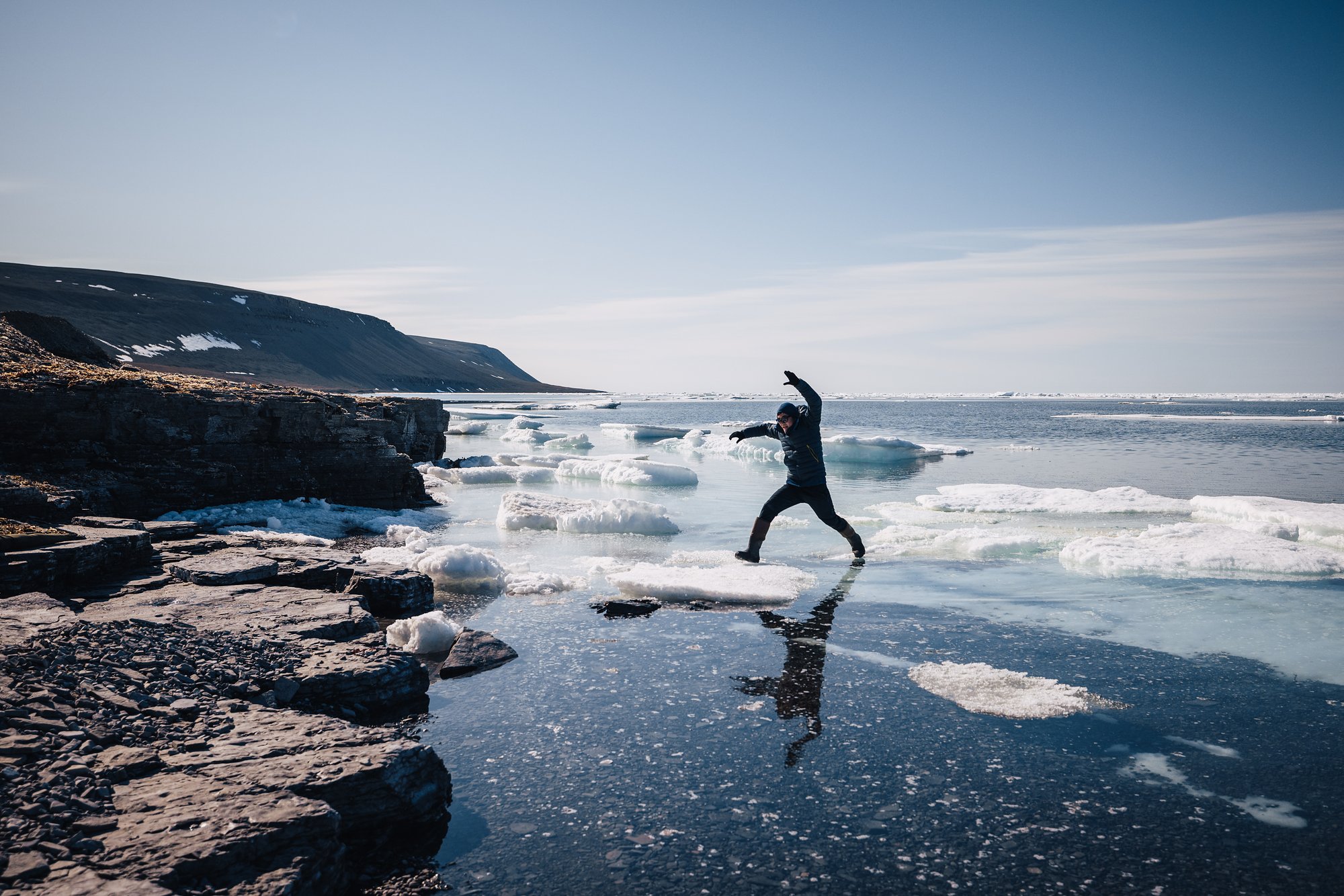 A guest leaping across the rocks at the water's edge, cliffs and floating ice behind