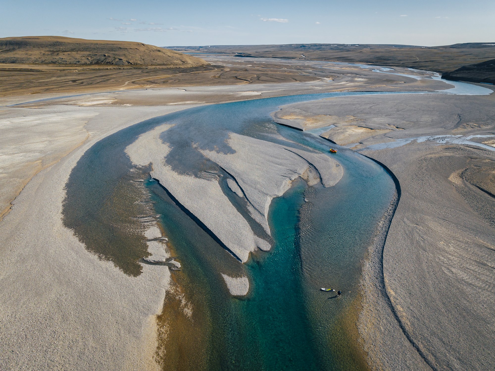Aerial view of a lone paddler on a teal braided channel between silver gravel bars