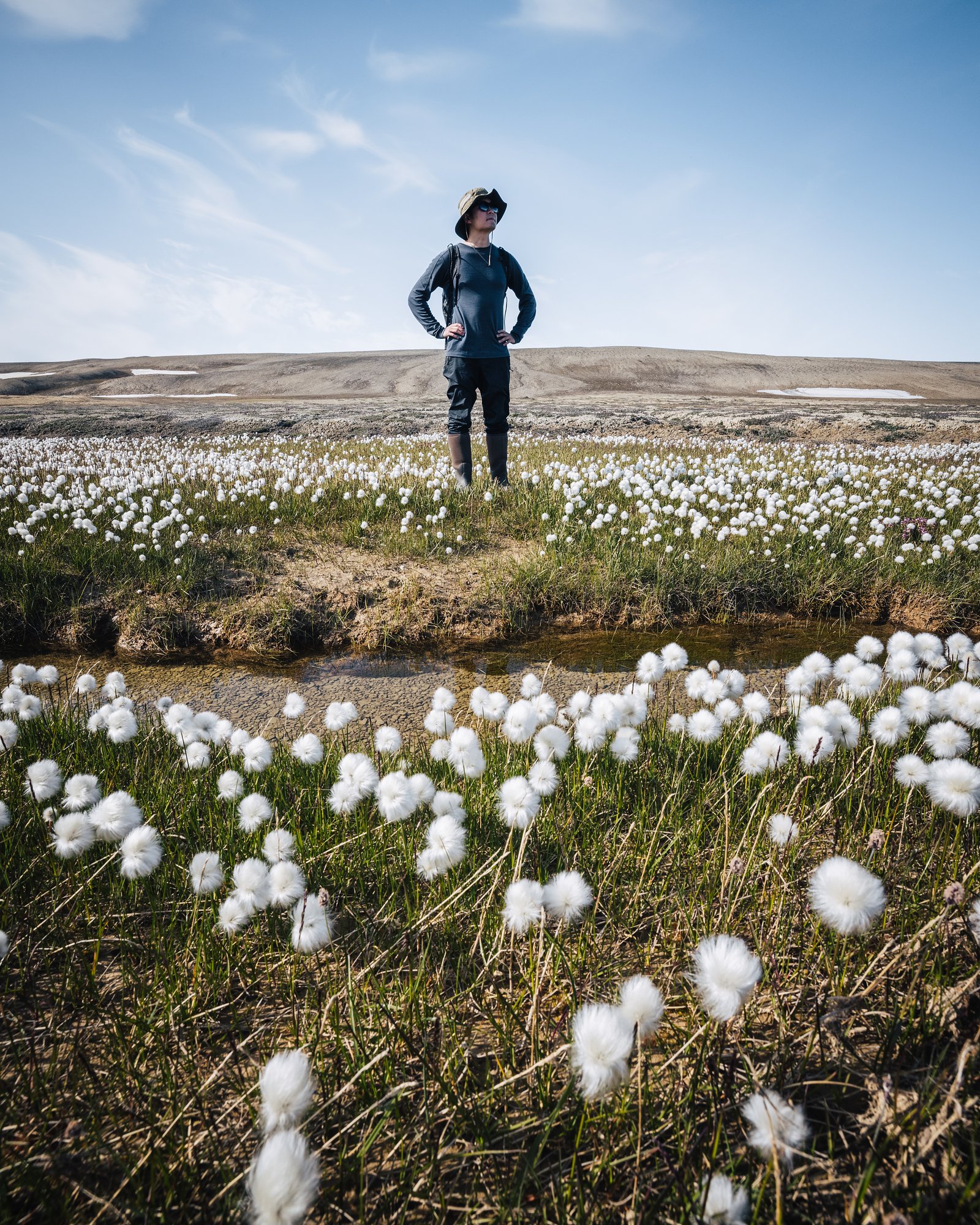 A paddler in a drysuit and cap standing among cottongrass on the tundra