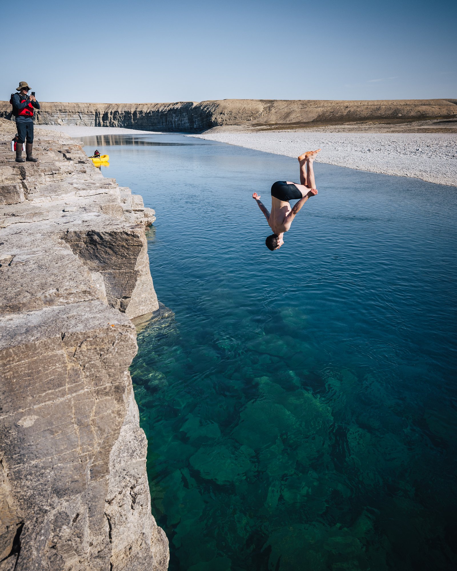 A guest backflipping off a limestone ledge into the teal Cunningham River while another watches from the edge