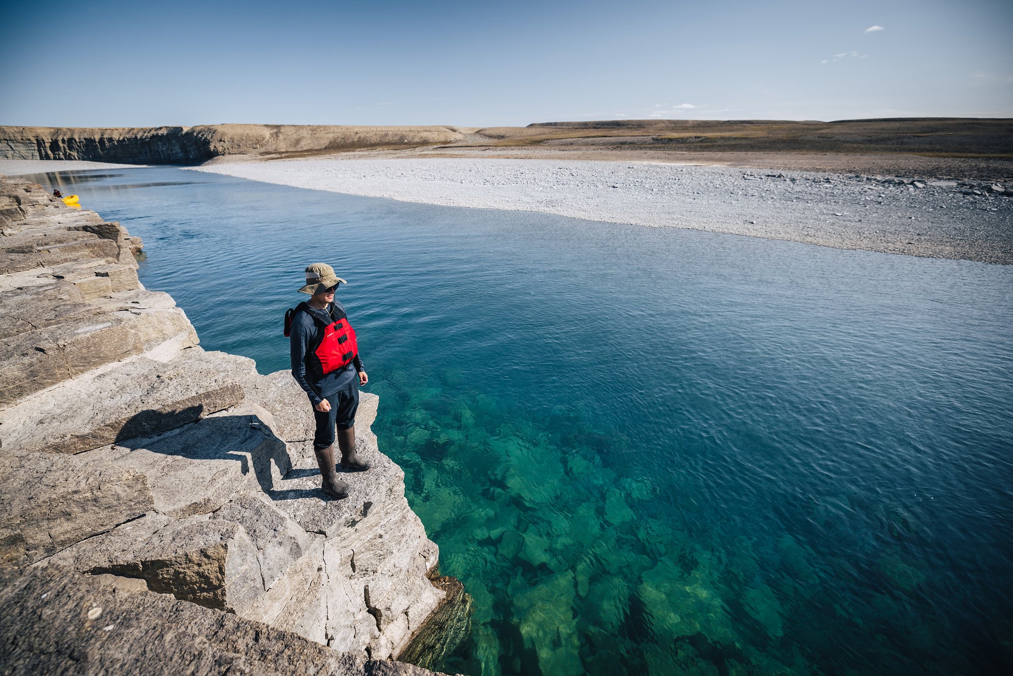 A guest in a red life jacket on a limestone ledge above clear teal water before the plunge