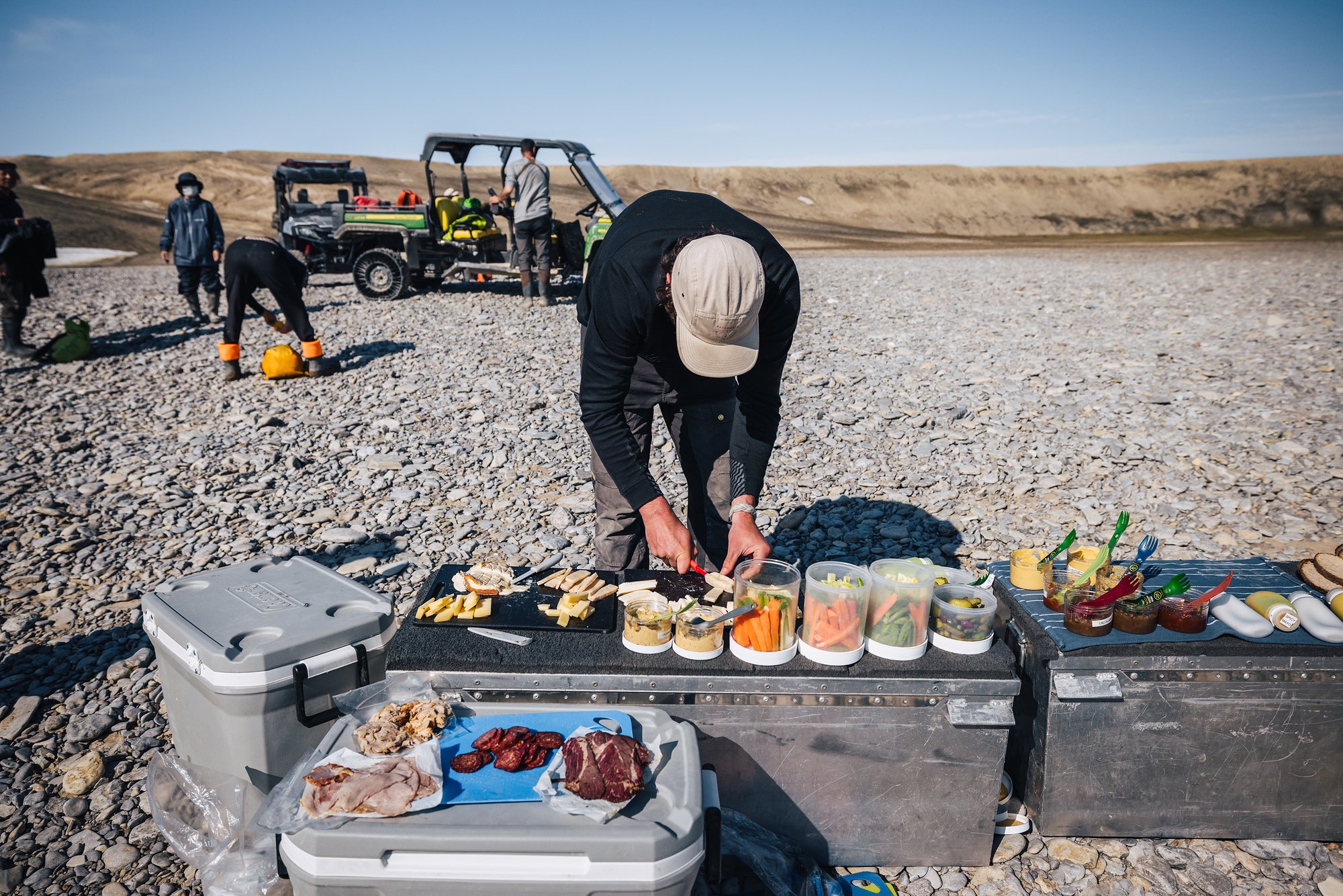 Riverside lunch laid out on equipment cases, buggies and guests behind