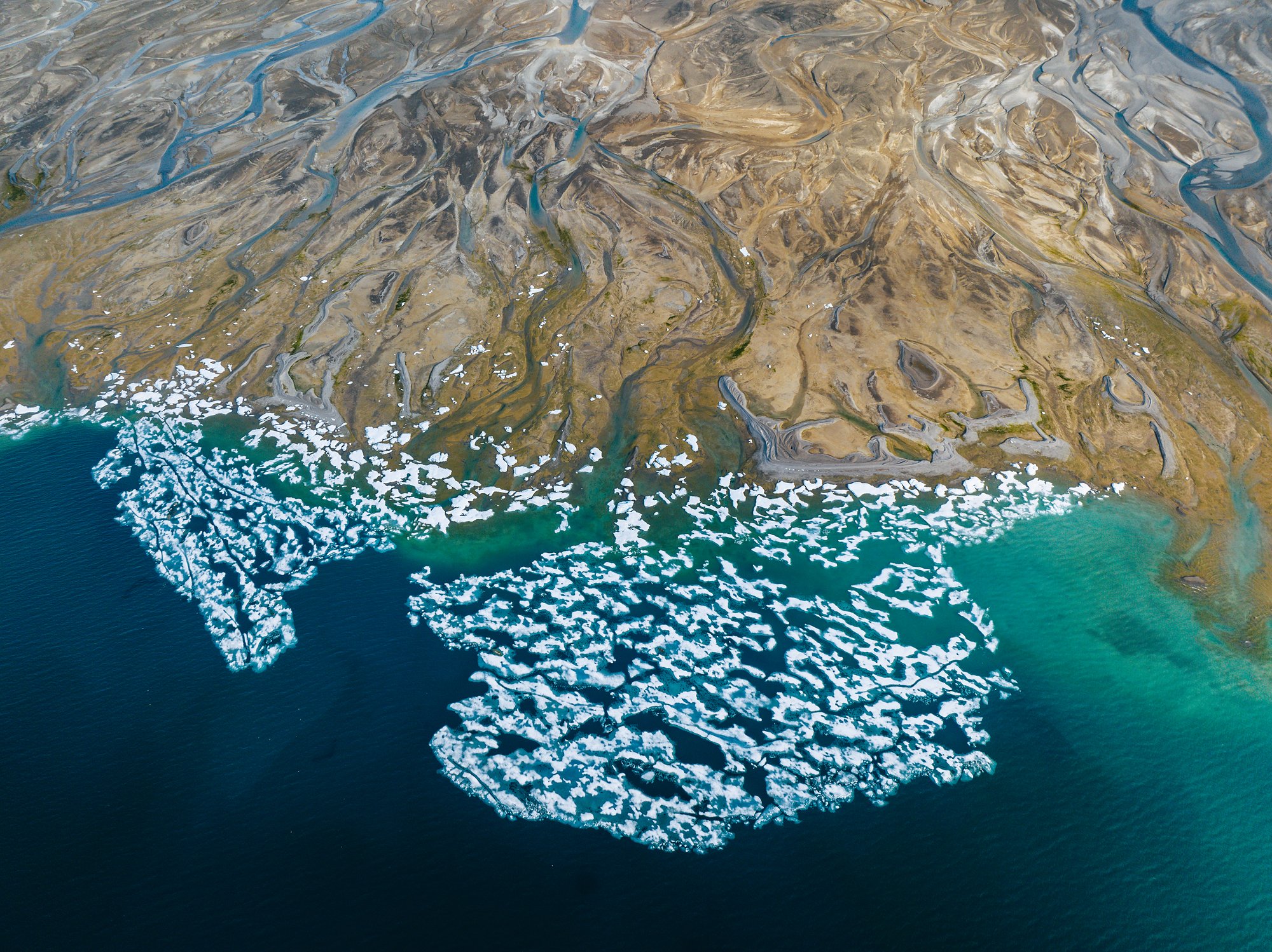 Aerial view of broken sea ice packed along the shore of Somerset Island, teal shallows and deep blue water