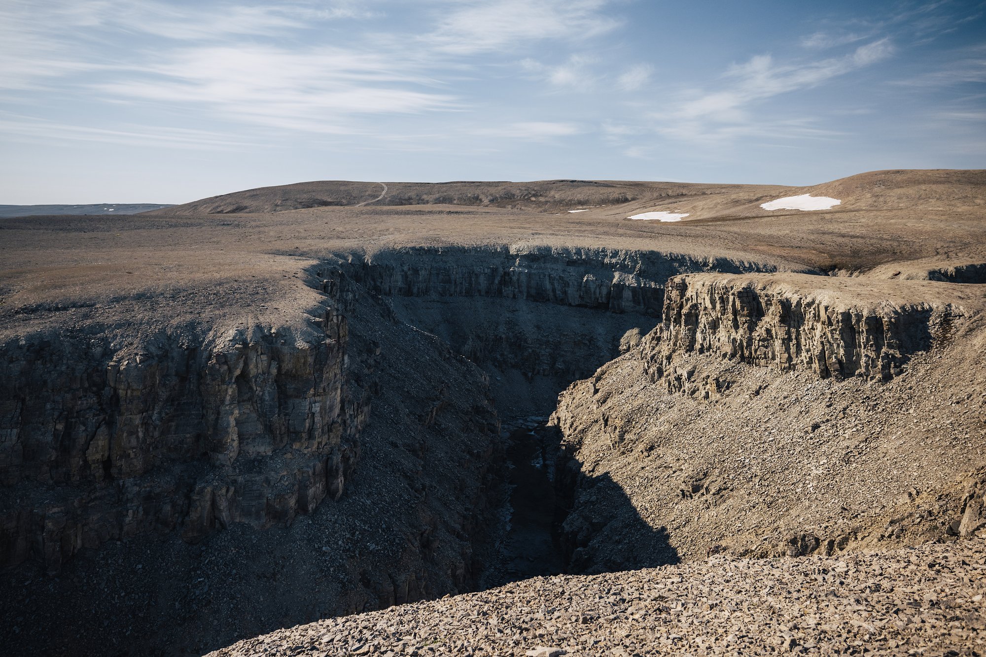 A deep canyon cut into the flat tundra plateau, snow patches on the ridge