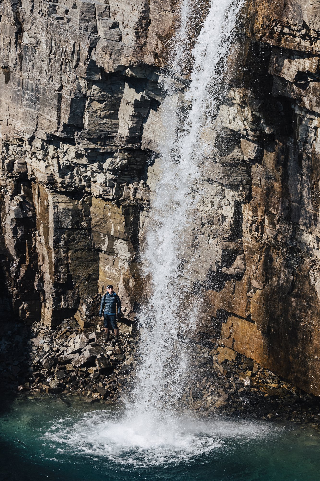 A tall waterfall plunging into a green pool, a small figure at its base for scale