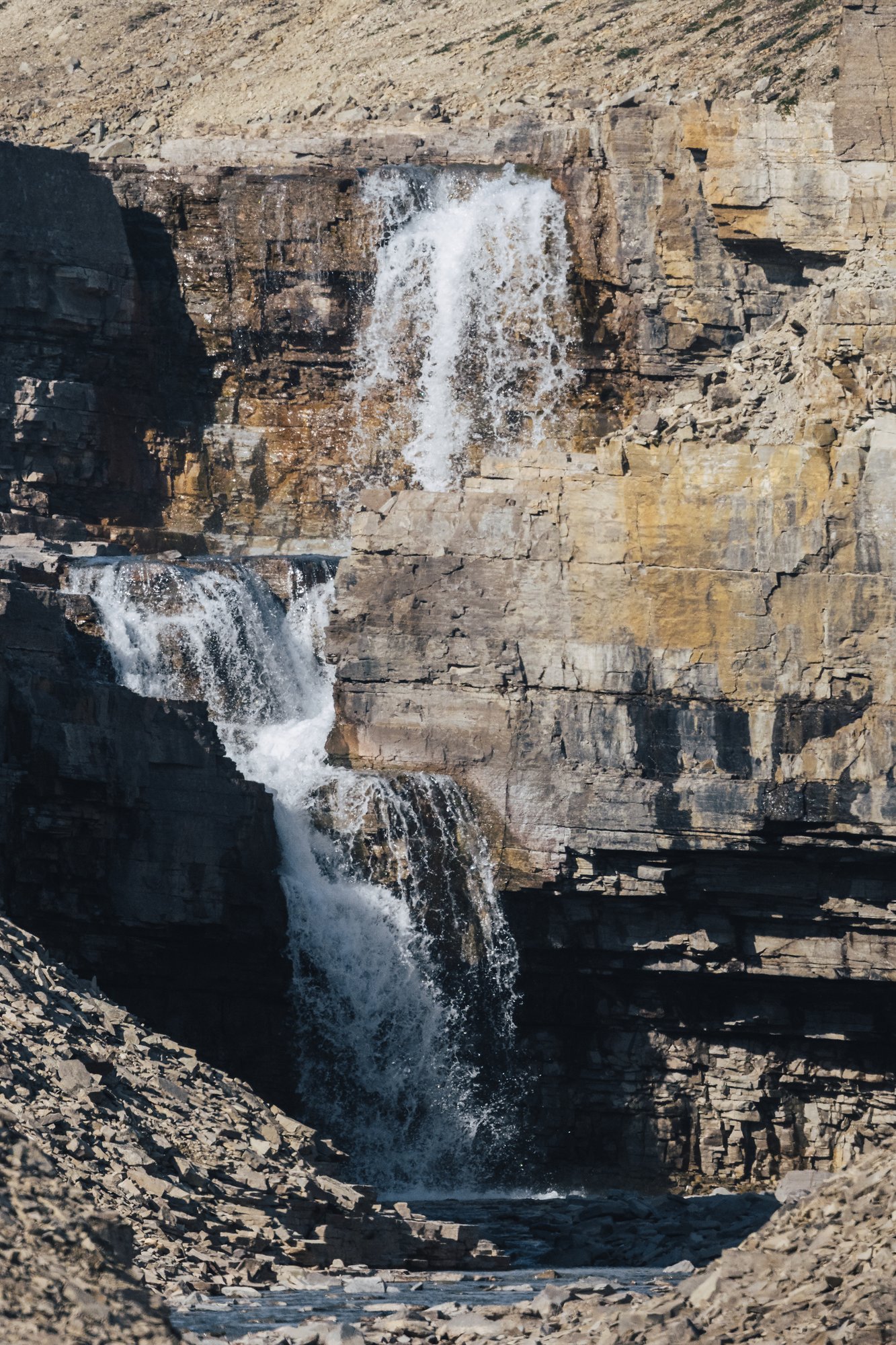 A two-tier waterfall cascading down a layered canyon wall