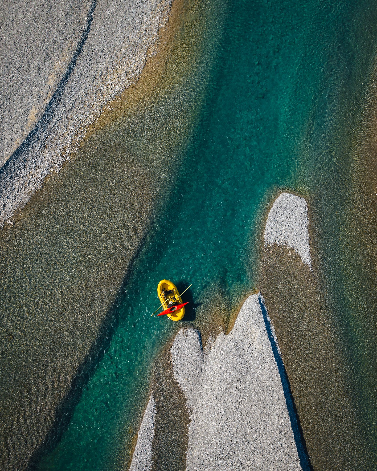 Aerial view of a yellow raft on a turquoise channel between white gravel bars