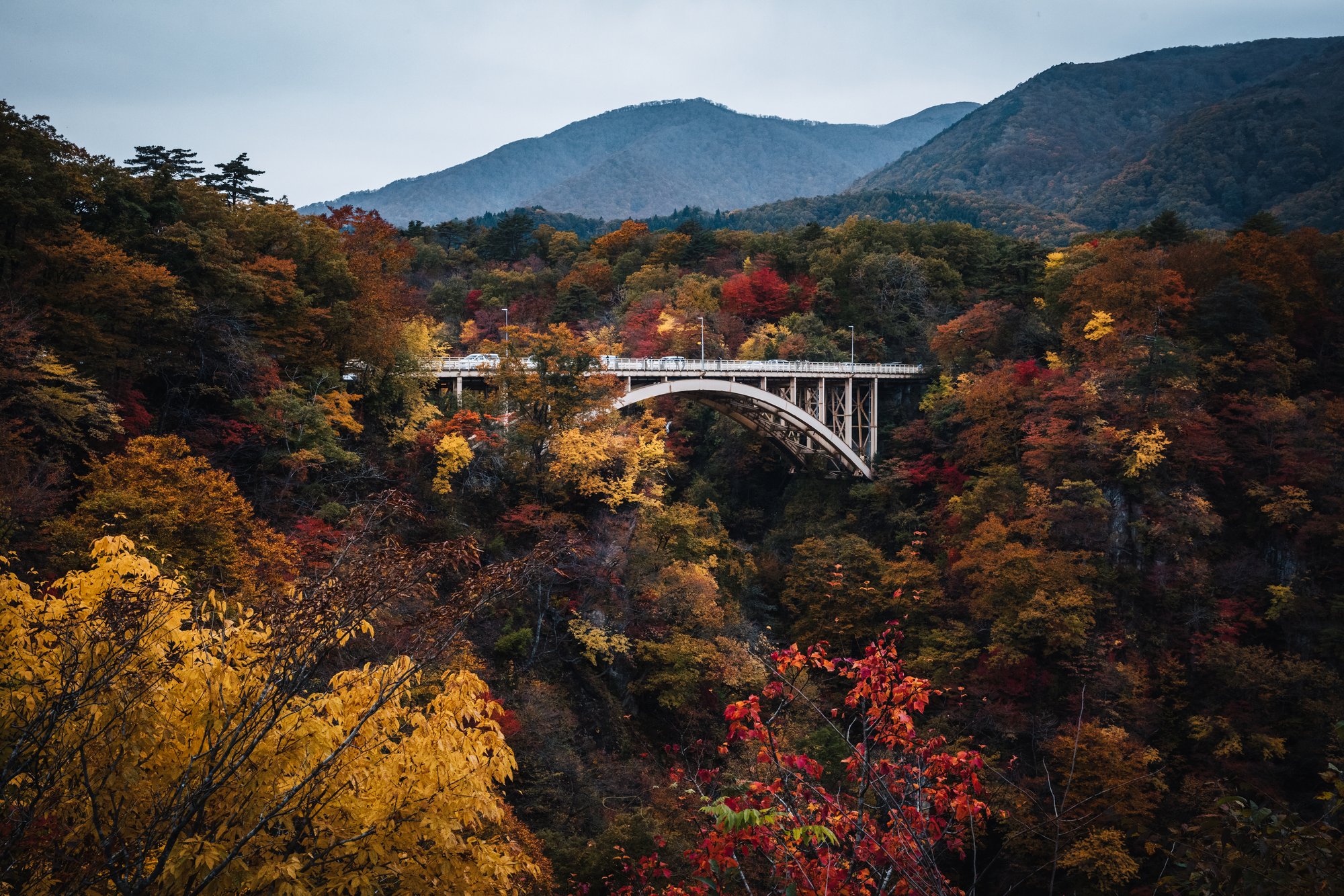 The Ofukazawa Bridge arching over Naruko Gorge with autumn-colored slopes and mountains behind