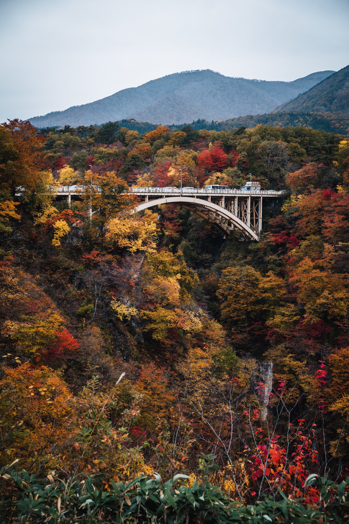 Cars crossing the Ofukazawa Bridge above Naruko Gorge with mountains beyond
