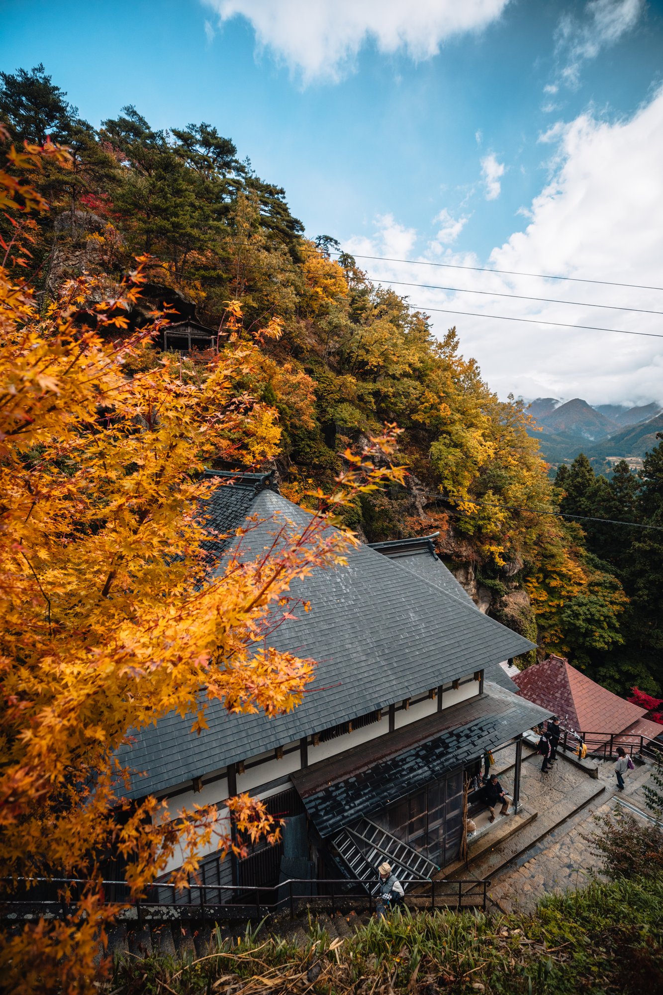 Temple hall roof beneath golden maple leaves at Yamadera with the valley beyond