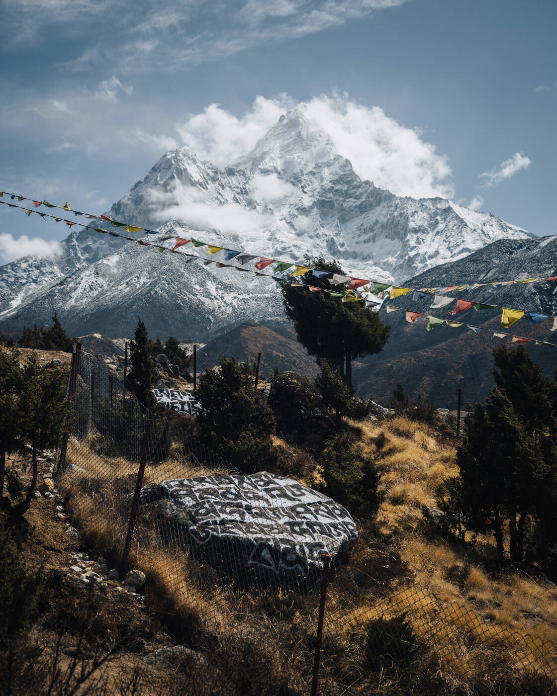 Ama Dablam framed between prayer flags and a painted mani stone on the ridge above Pangboche