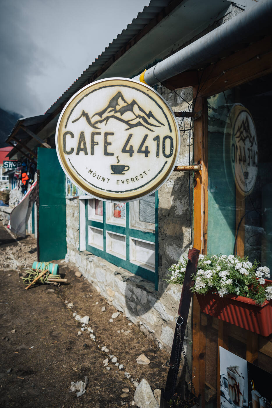 The Cafe 4410 sign in Dingboche — a round mountain-logo marquee with ~MOUNT EVEREST~ painted below, flower boxes at the entrance