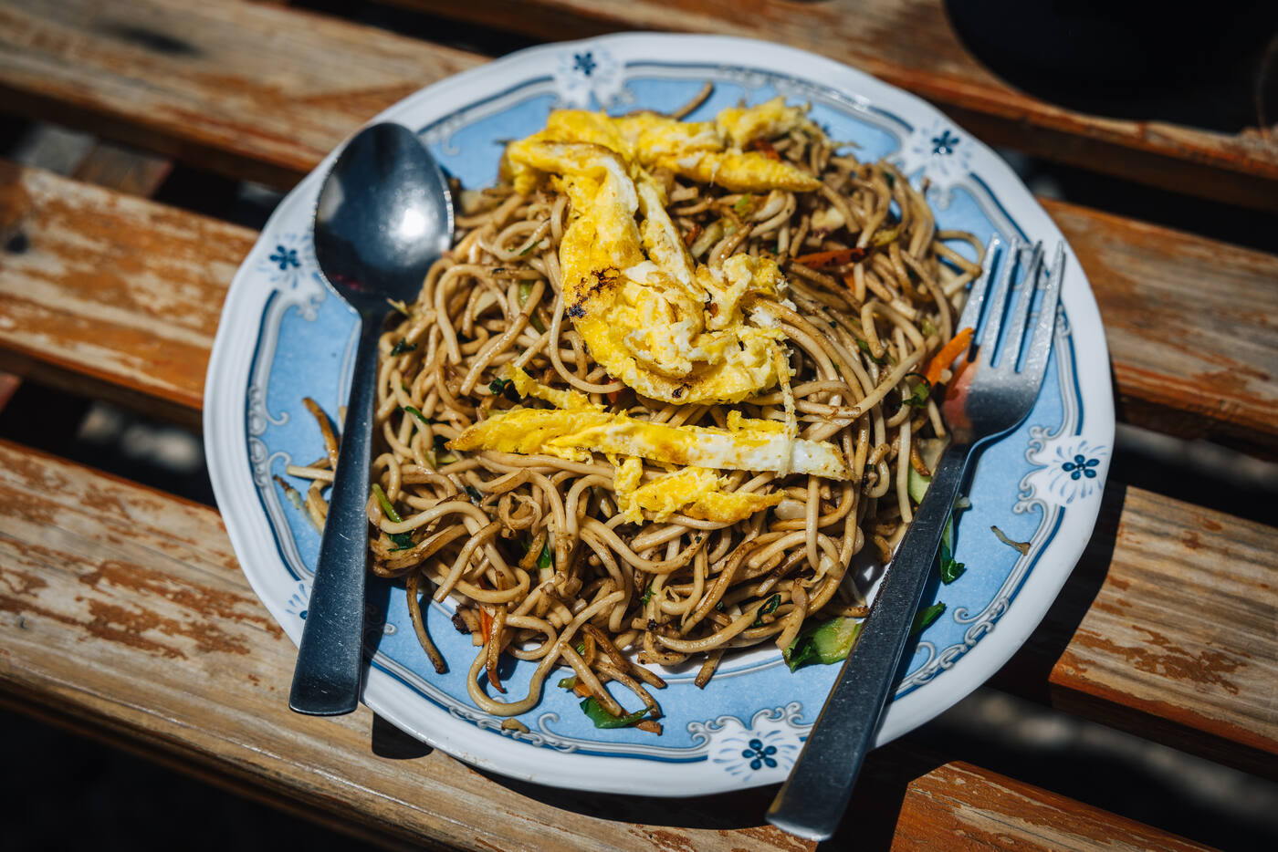 A heaped plate of Nepali chow mein with egg on a blue-floral ceramic plate — lodge lunch fuel on rest day