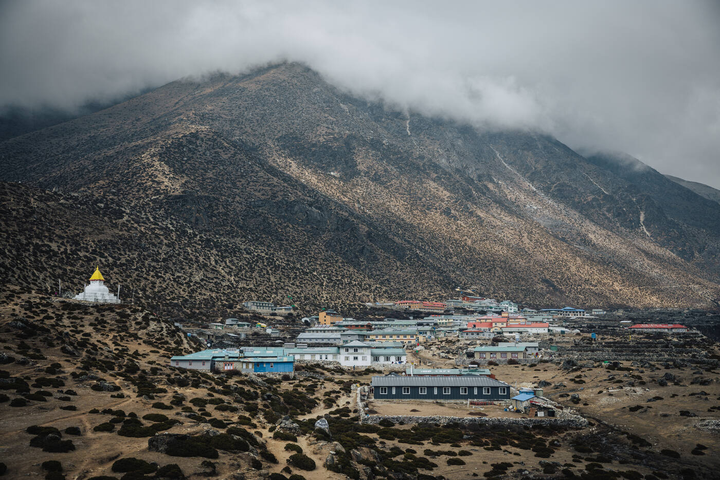 Dingboche village from above, a white stupa on the left and cloud-draped peaks behind the stone lodges