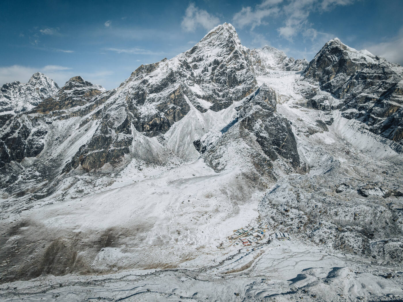 Drone view of a snow-blanketed Cholatse / Taboche massif with tiny colorful Lobuche lodges huddled at the base