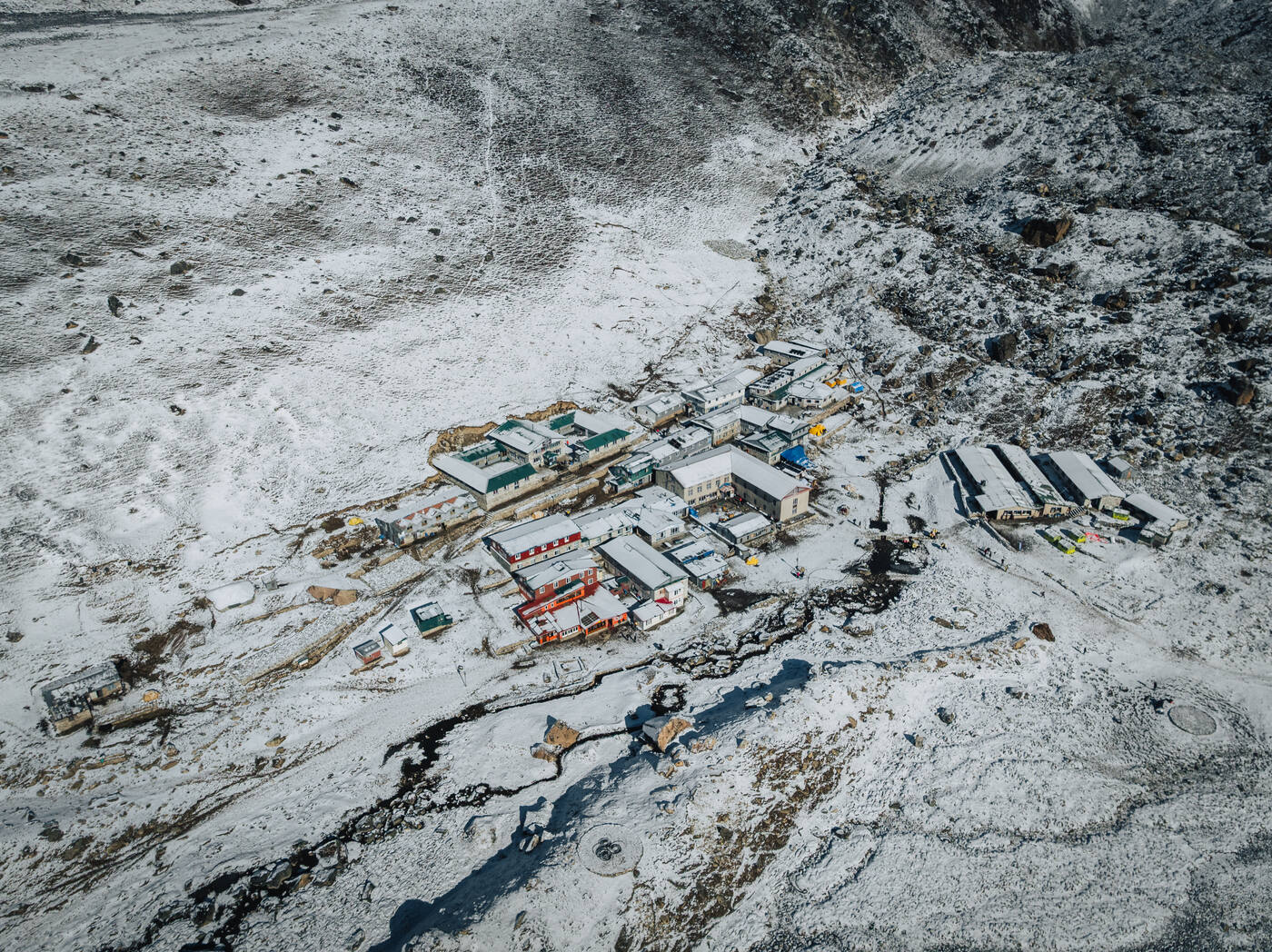Drone aerial of Gorak Shep village — colorful rooftops huddled on the snowy glacial plateau