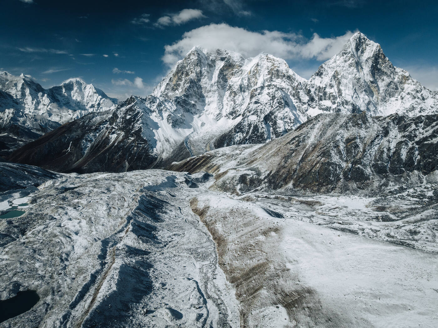 Drone aerial of the Khumbu Glacier — a snow-streaked rock pavement curving toward jagged 6,000m peaks on the horizon