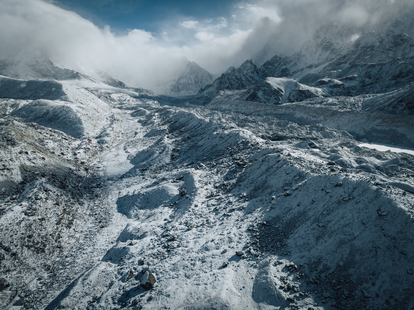 Drone aerial of the Khumbu Glacier ice and rock surface after fresh snow — corrugated patterns of moraine stretching toward Pumori