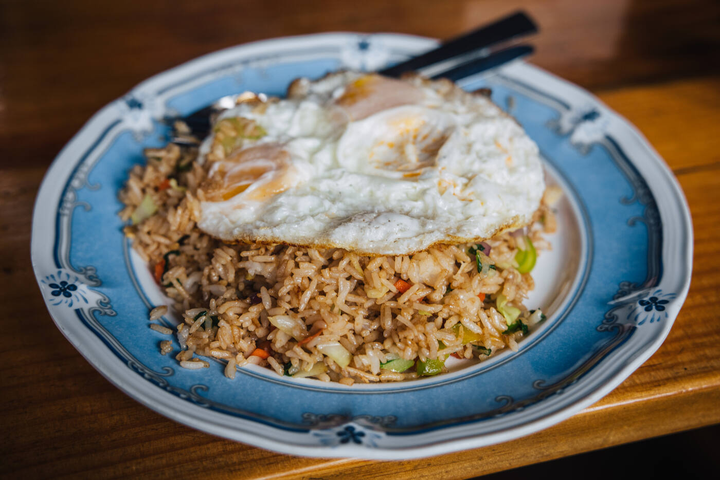 Vegetable fried rice topped with two fried eggs on a blue-rimmed china plate — a teahouse meal at altitude