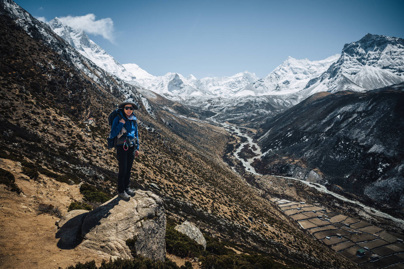 Grace standing on a rocky outcrop above the Dingboche valley, a panorama of snow peaks stretching to the horizon